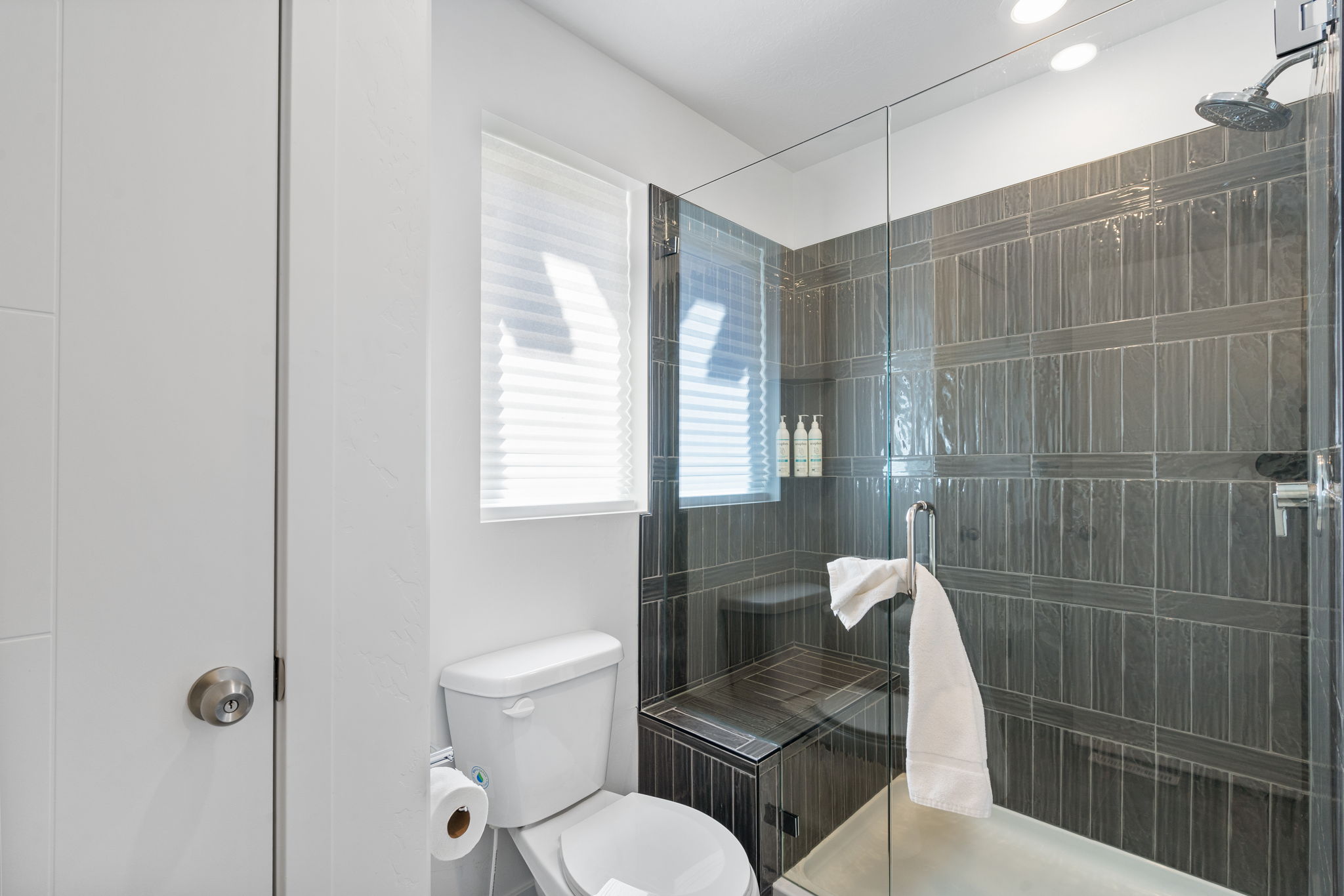 Modern bathroom featuring a glass-enclosed shower with dark vertical tile, an integrated shower bench, and a rainfall shower head