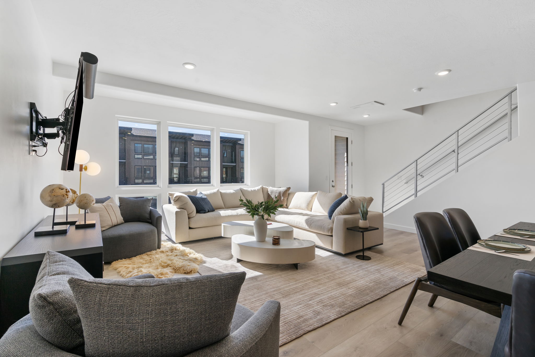 Open-concept living area featuring light wood-finish flooring, recessed lighting, and a modern staircase with cable railings