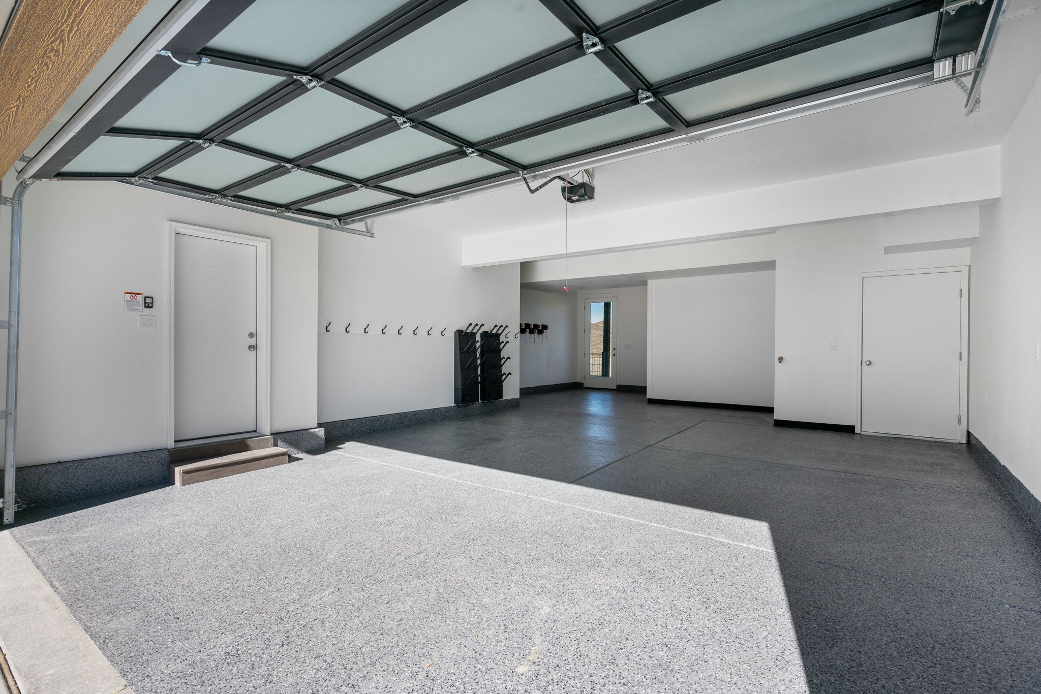 Spacious garage featuring a frosted panel garage door, epoxy floor, white painted walls, and built-in wall hooks