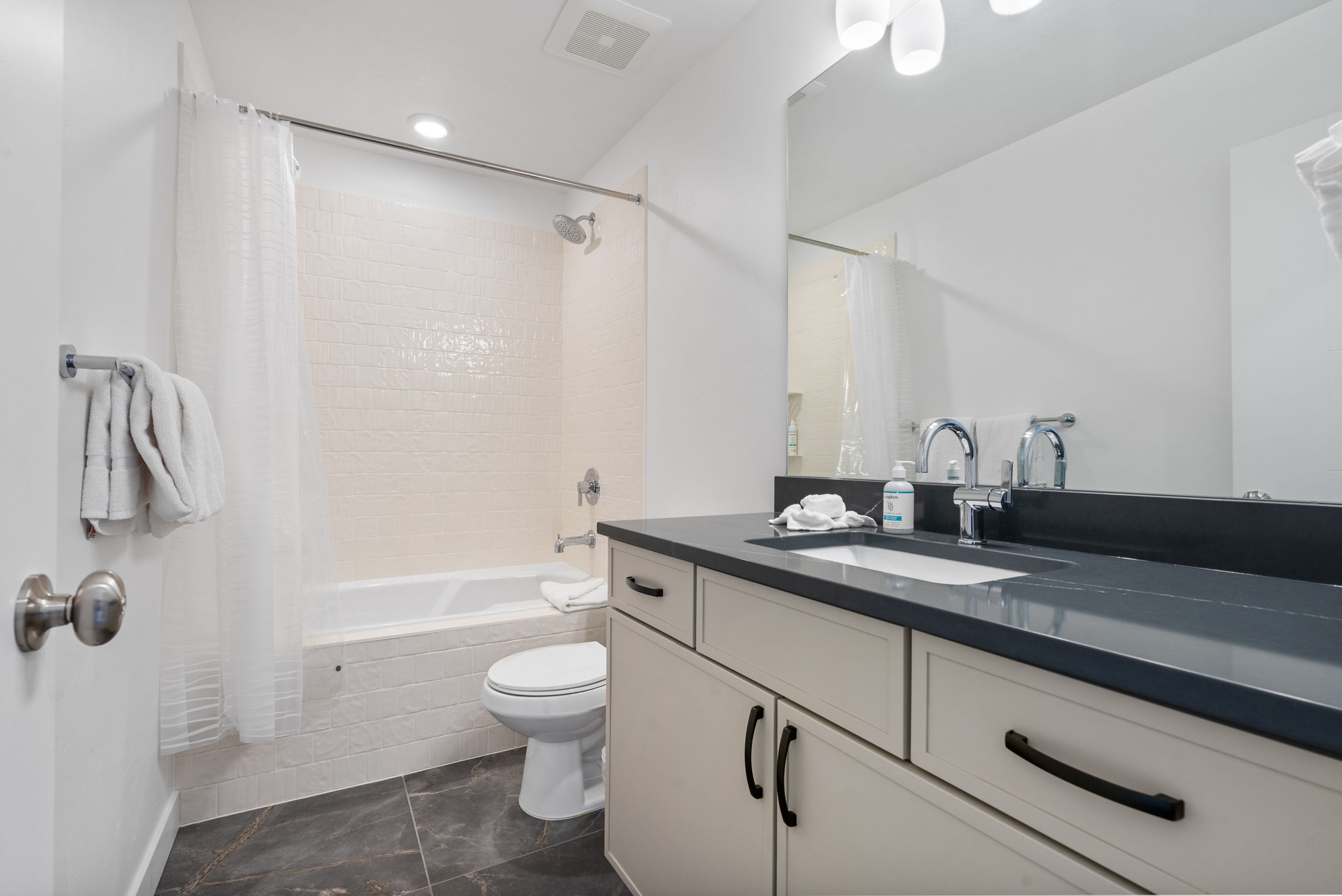 Bathroom featuring a vanity with an integrated sink, dark countertop, and light cabinetry with dark hardware