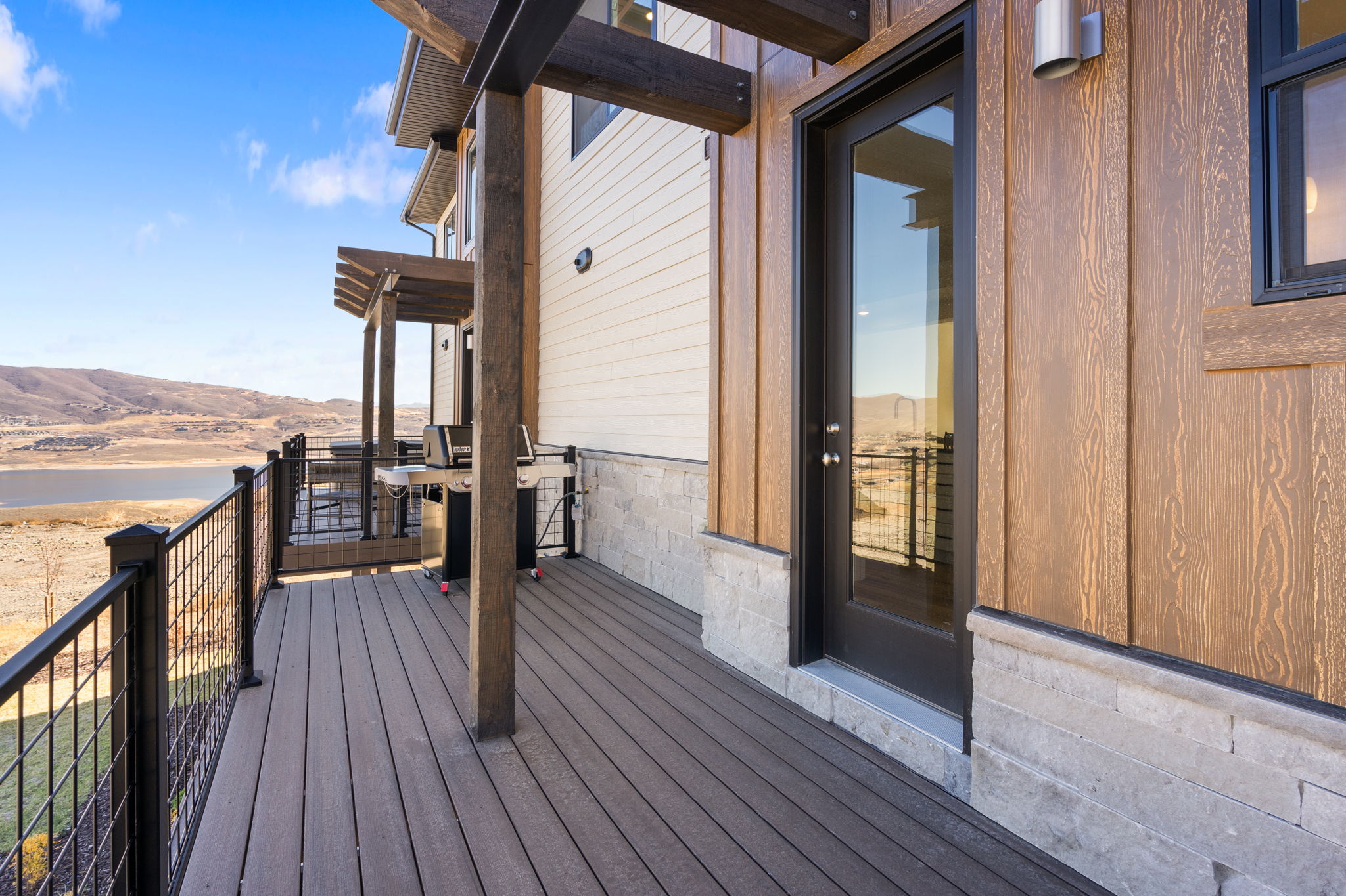 Expansive outdoor deck featuring composite decking, dark wood structural pergola, and black metal grid railing