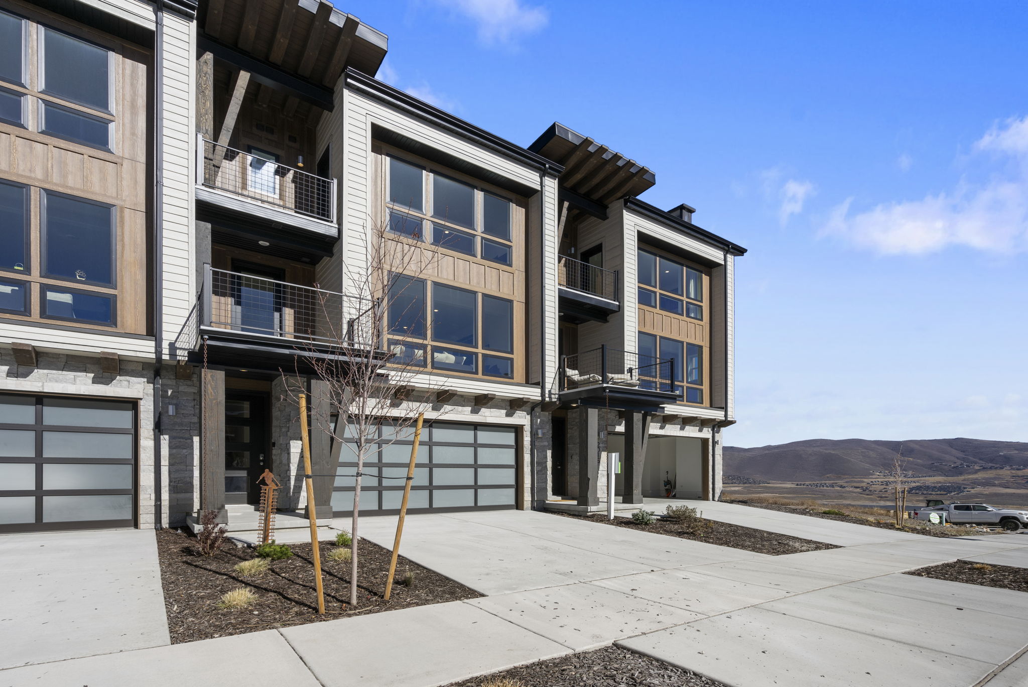 Modern townhome exterior featuring an integrated garage, large windows, multiple balconies, and mixed material siding