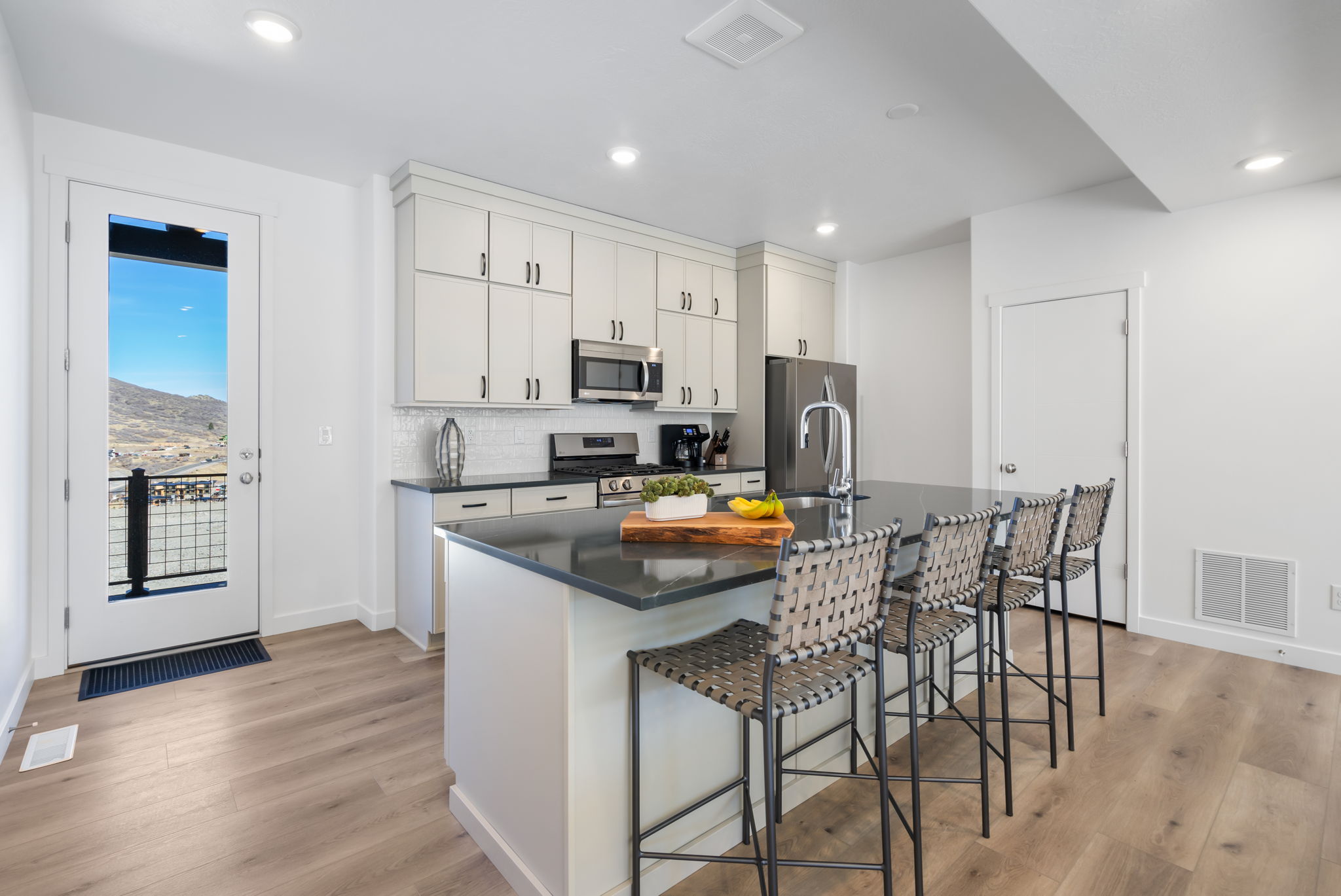 Modern kitchen featuring light-toned cabinetry, dark countertops, stainless steel appliances, and a white subway tile backsplash