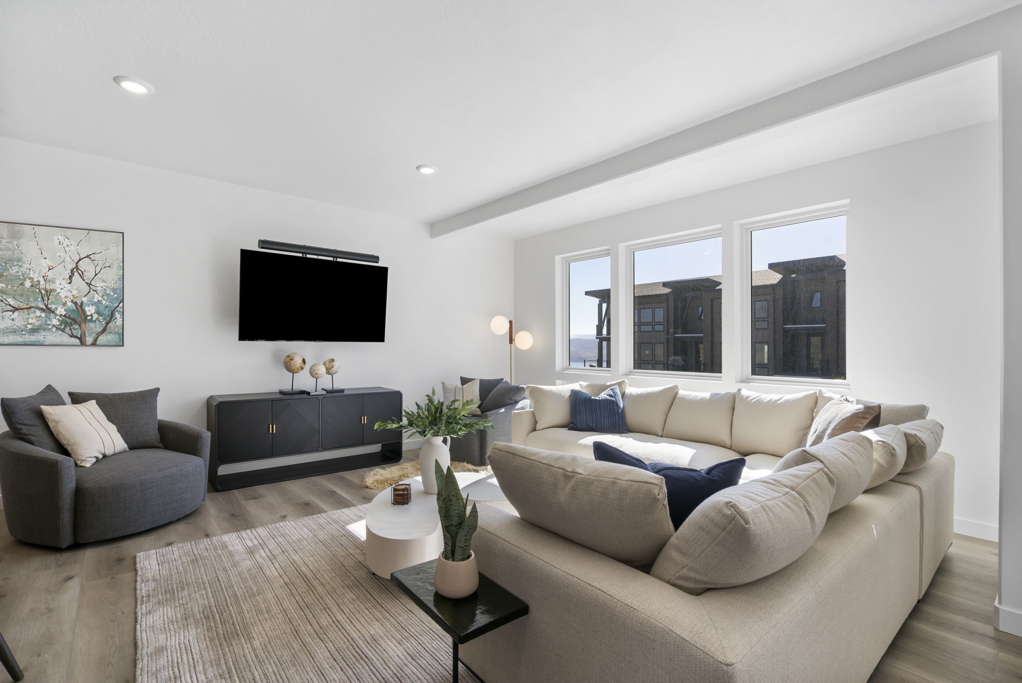 Spacious living area featuring light wood-finish flooring, recessed lighting, and large windows providing ample natural light