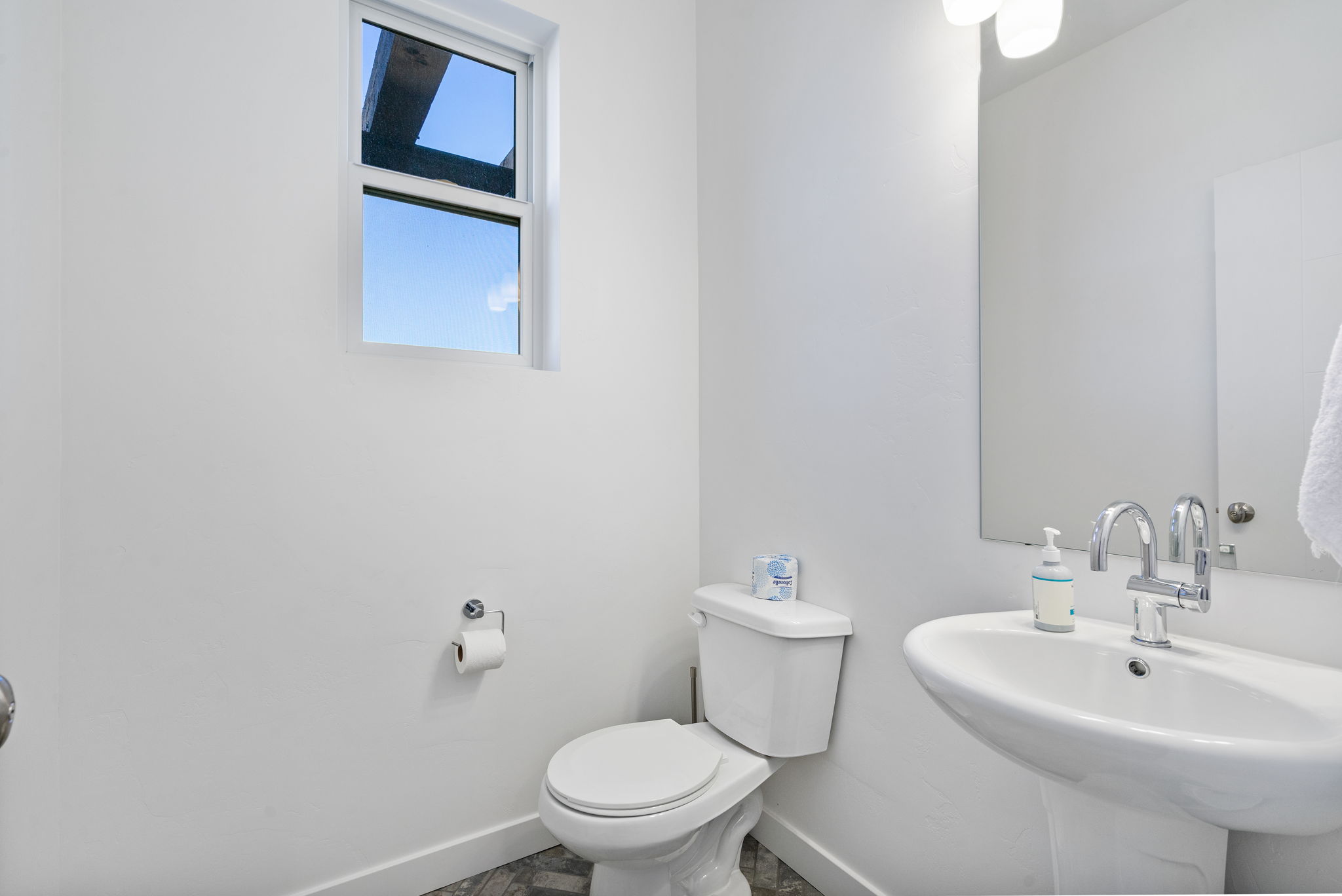 Bathroom featuring a pedestal sink with chrome faucet, a white toilet, and a rectangular window