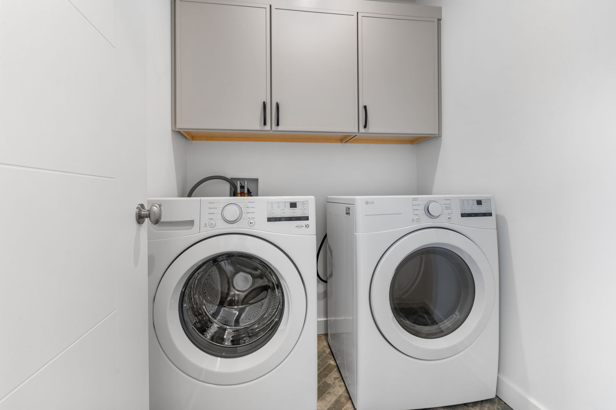Laundry area featuring stacked front-load machines, light gray upper cabinetry with black hardware, and wood-finish flooring