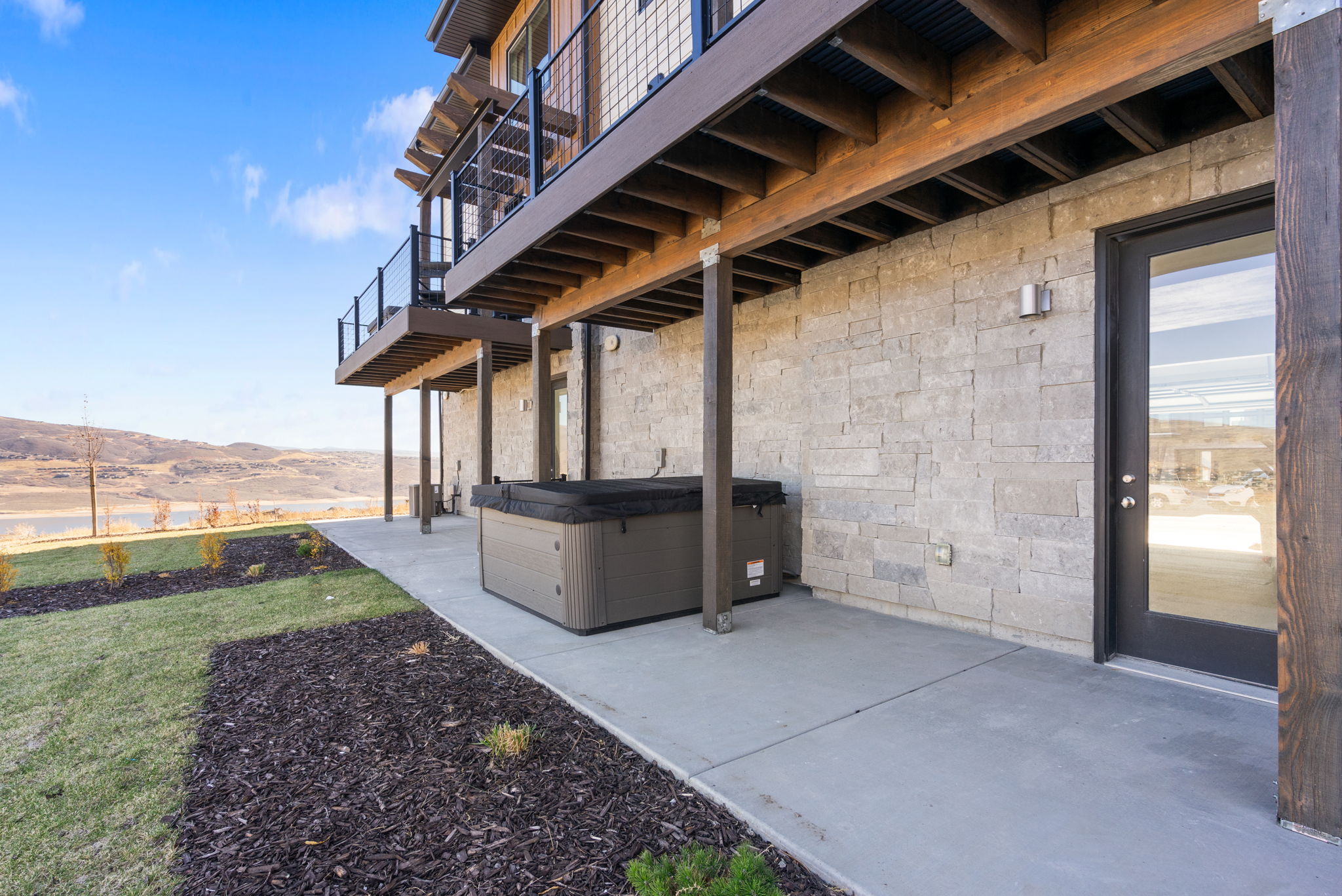 Lower-level patio featuring a spa, concrete flooring, and stone-finish exterior