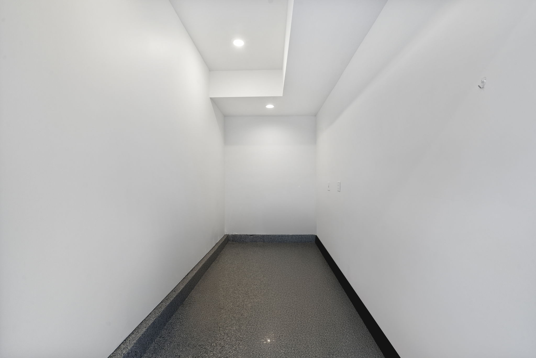 Recessed lighting illuminates a space featuring a contrasting baseboard and speckled flooring