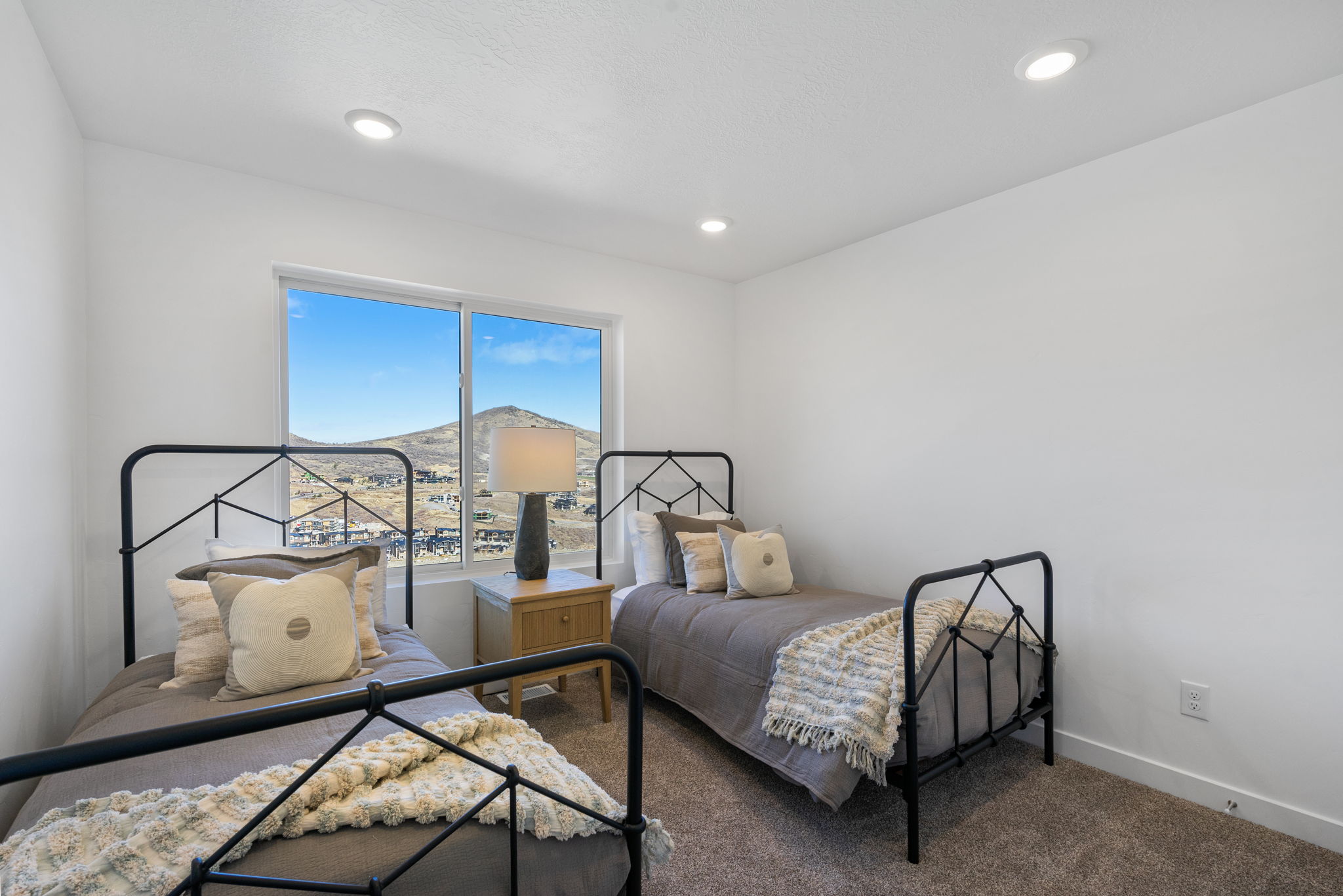 Spacious bedroom featuring plush carpeting, recessed lighting, and a large window framing distant mountain and community scenery