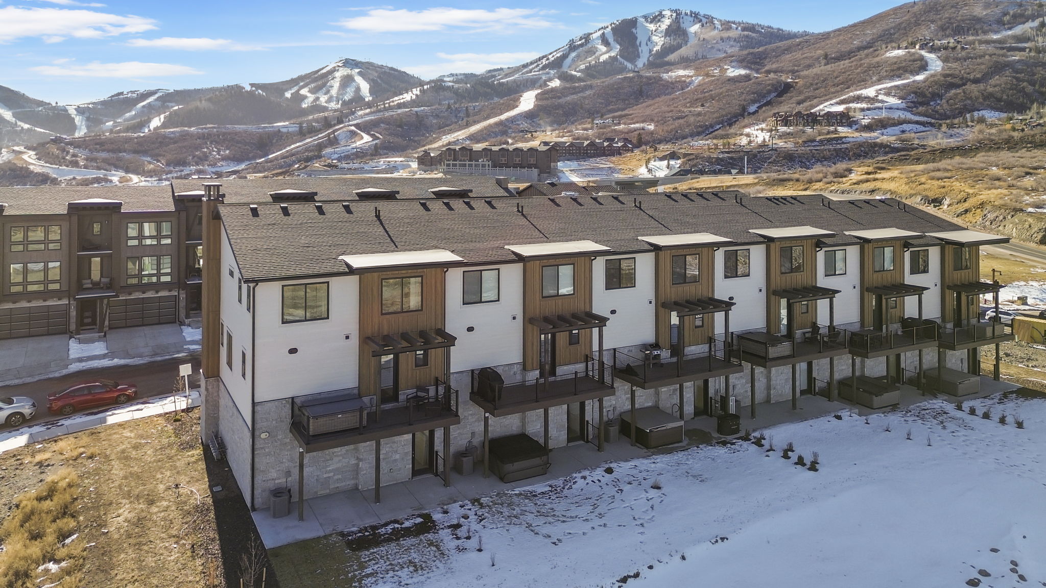 Modern townhome with multi-level decks and integrated hot tubs, featuring a mountain backdrop