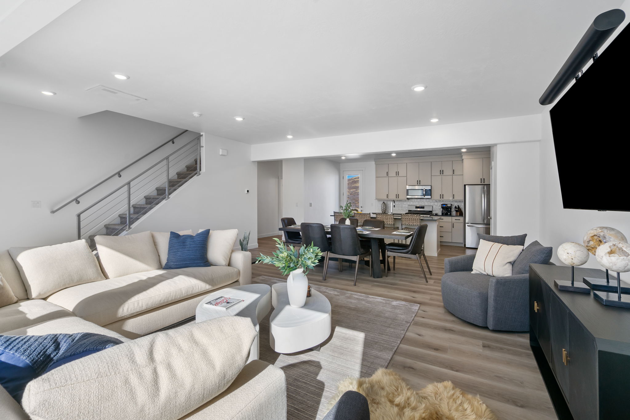 Open-concept living area featuring wood-finish flooring, recessed lighting, and a modern cable railing staircase
