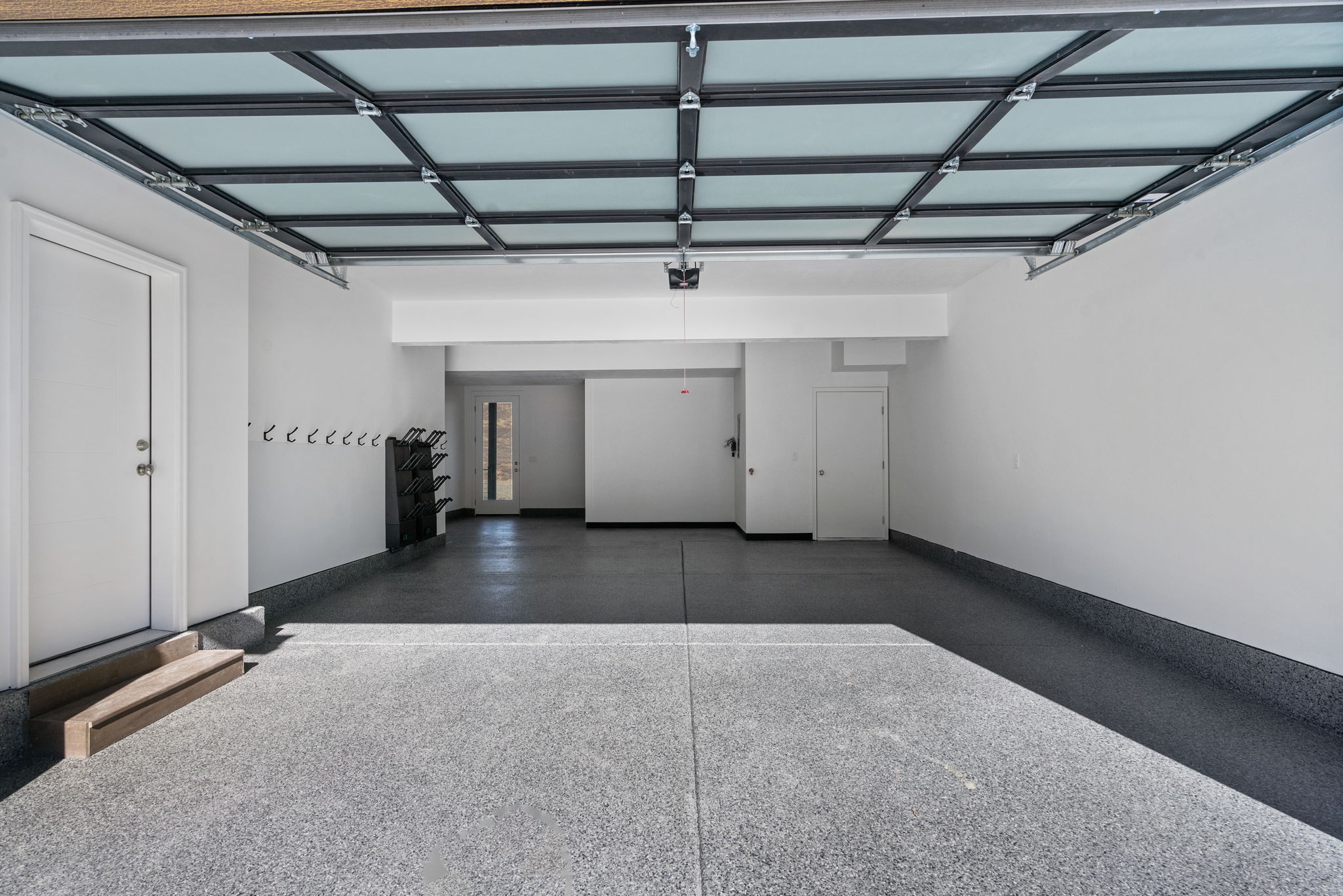 Spacious garage featuring an epoxy floor finish, a translucent panel garage door, white painted walls, and built-in wall hooks