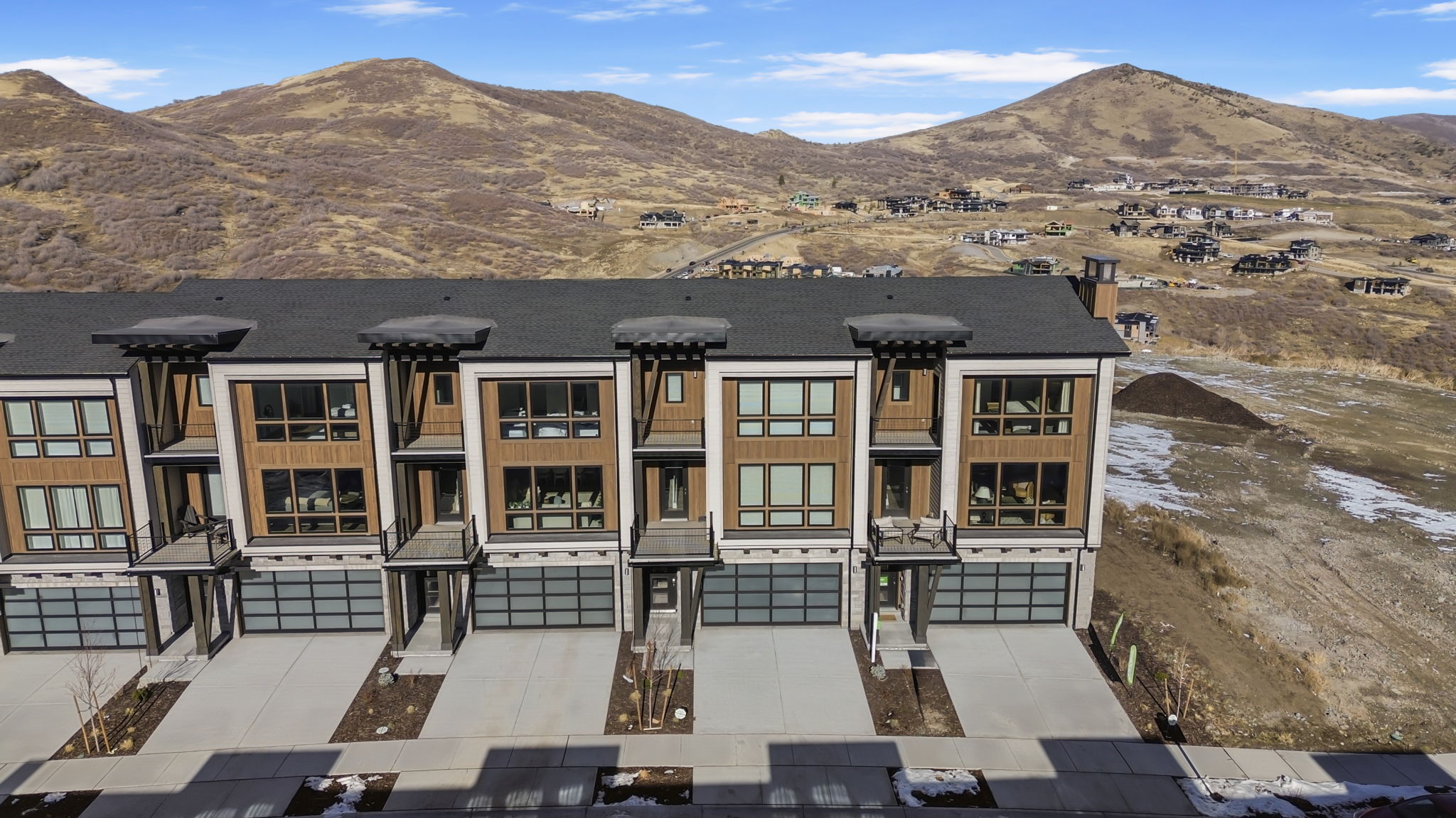 Modern townhome exteriors featuring wood-look siding, large windows, and a dark shingle roof