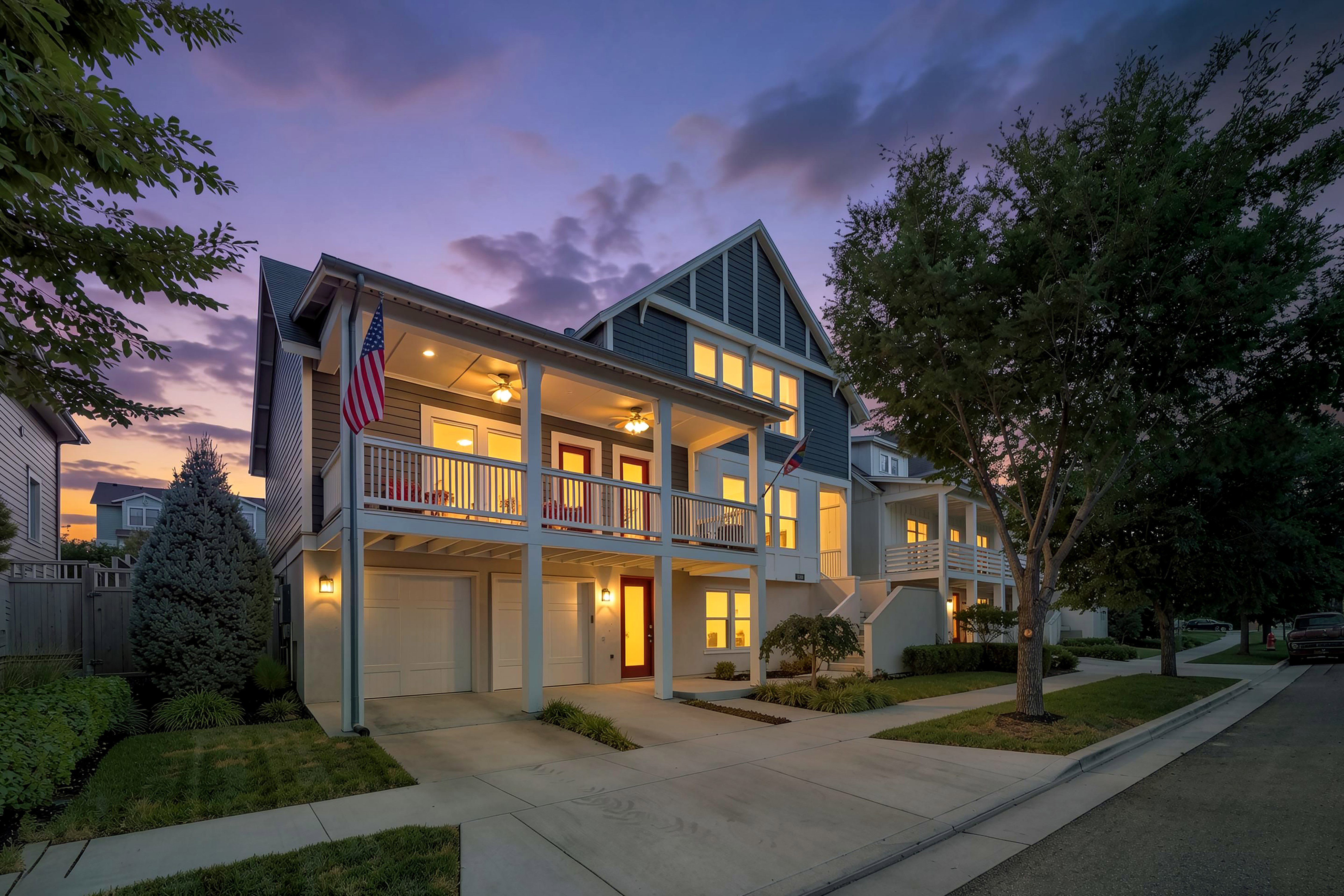 Two-story residential exterior featuring a covered balcony, integrated garage, and a red entry door