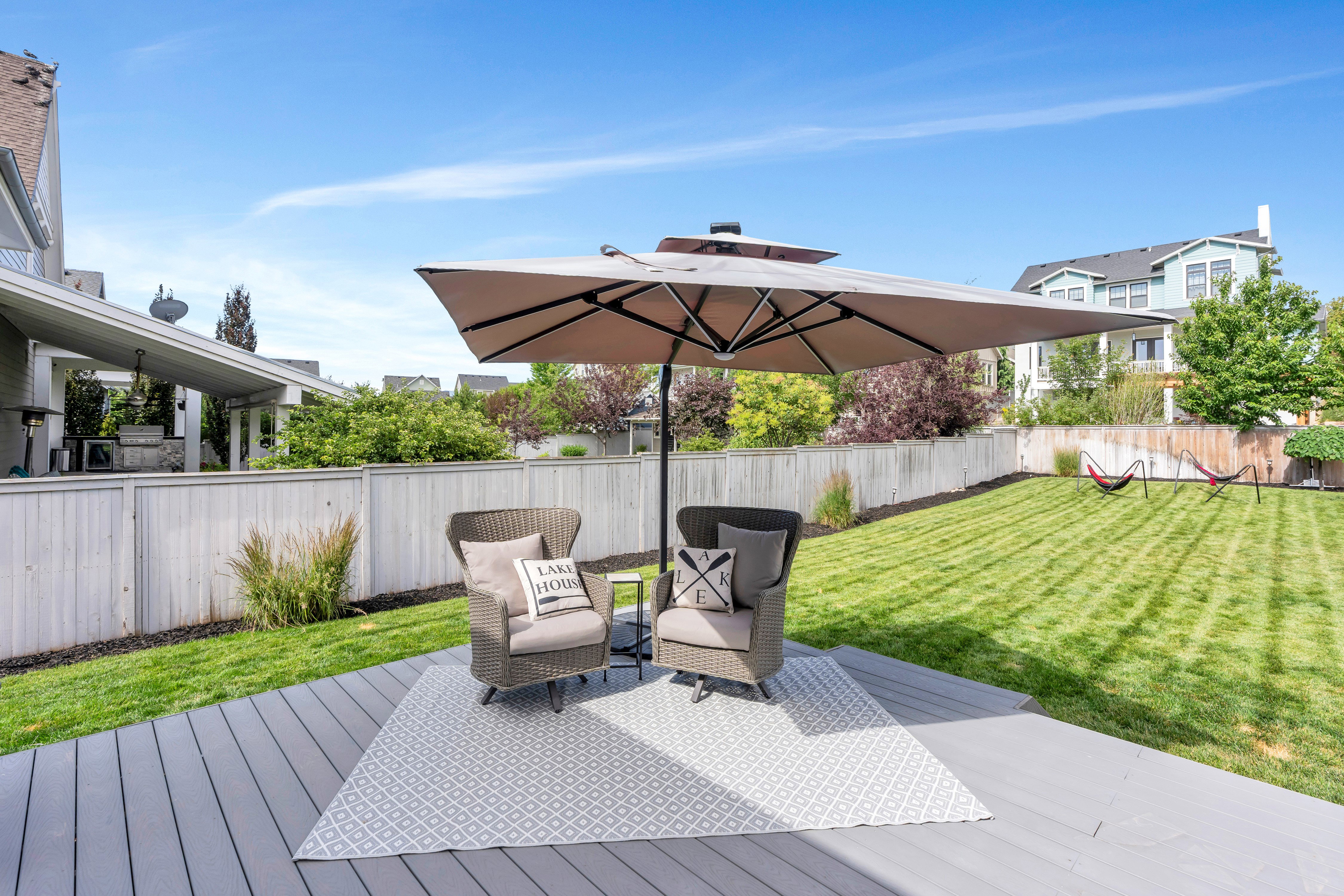 Expansive backyard featuring a gray composite deck, green lawn, white privacy fencing, and mature landscaping