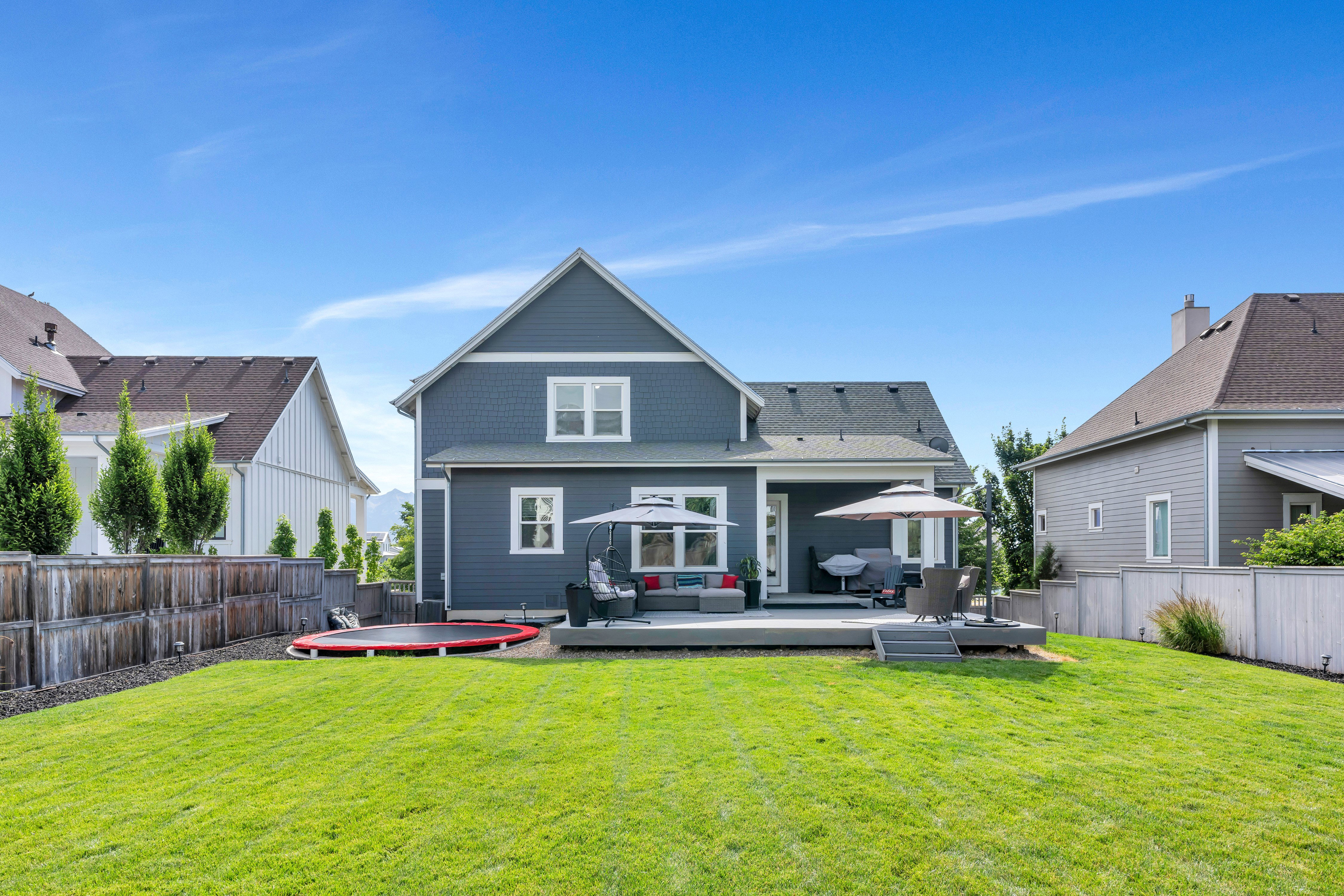 Expansive green lawn with a spacious outdoor deck, covered patio area, and perimeter fencing