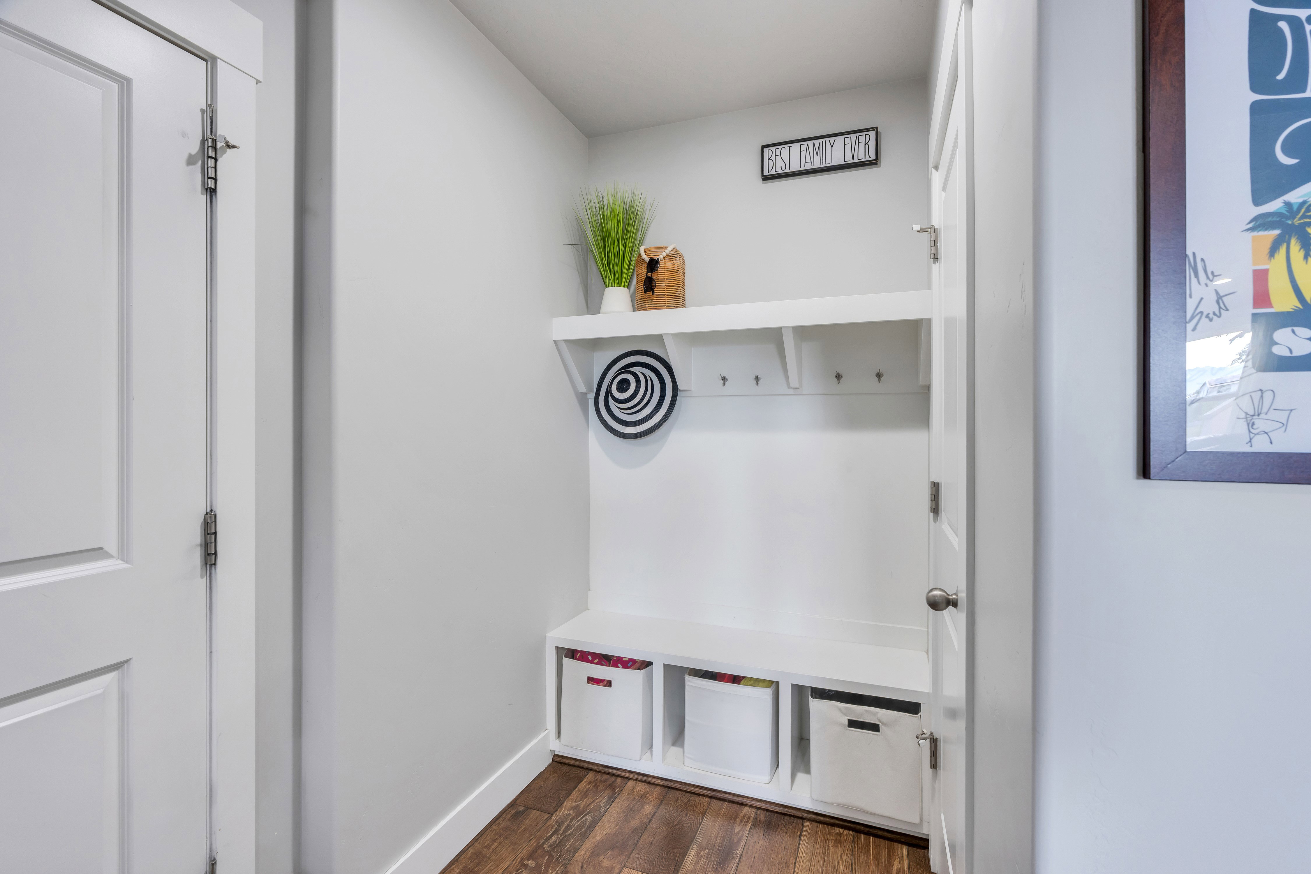 Built-in white storage bench with open cubbies, a white shelf, and coat hooks