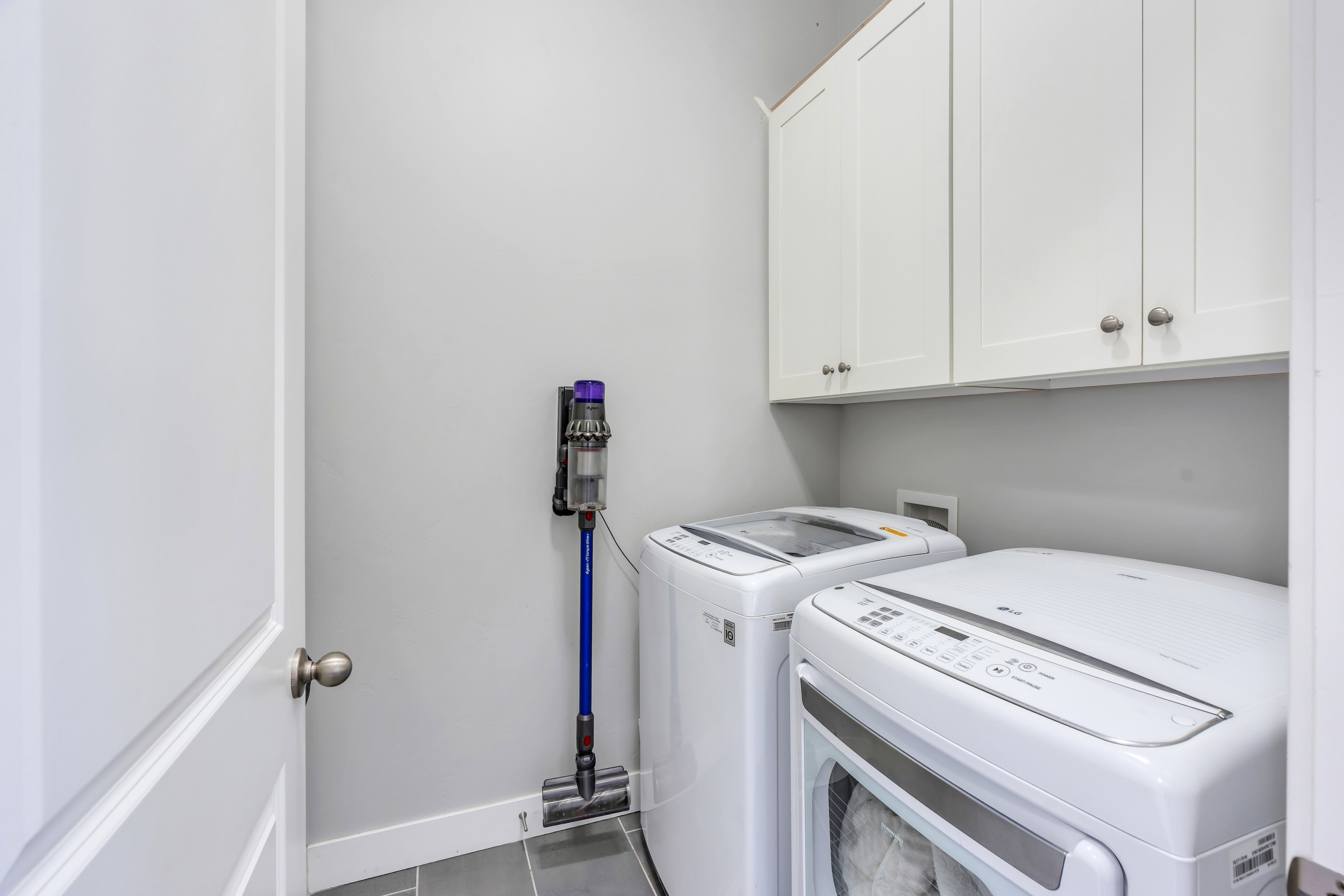 Laundry area with white cabinetry, gray wall paint, and gray floor tile
