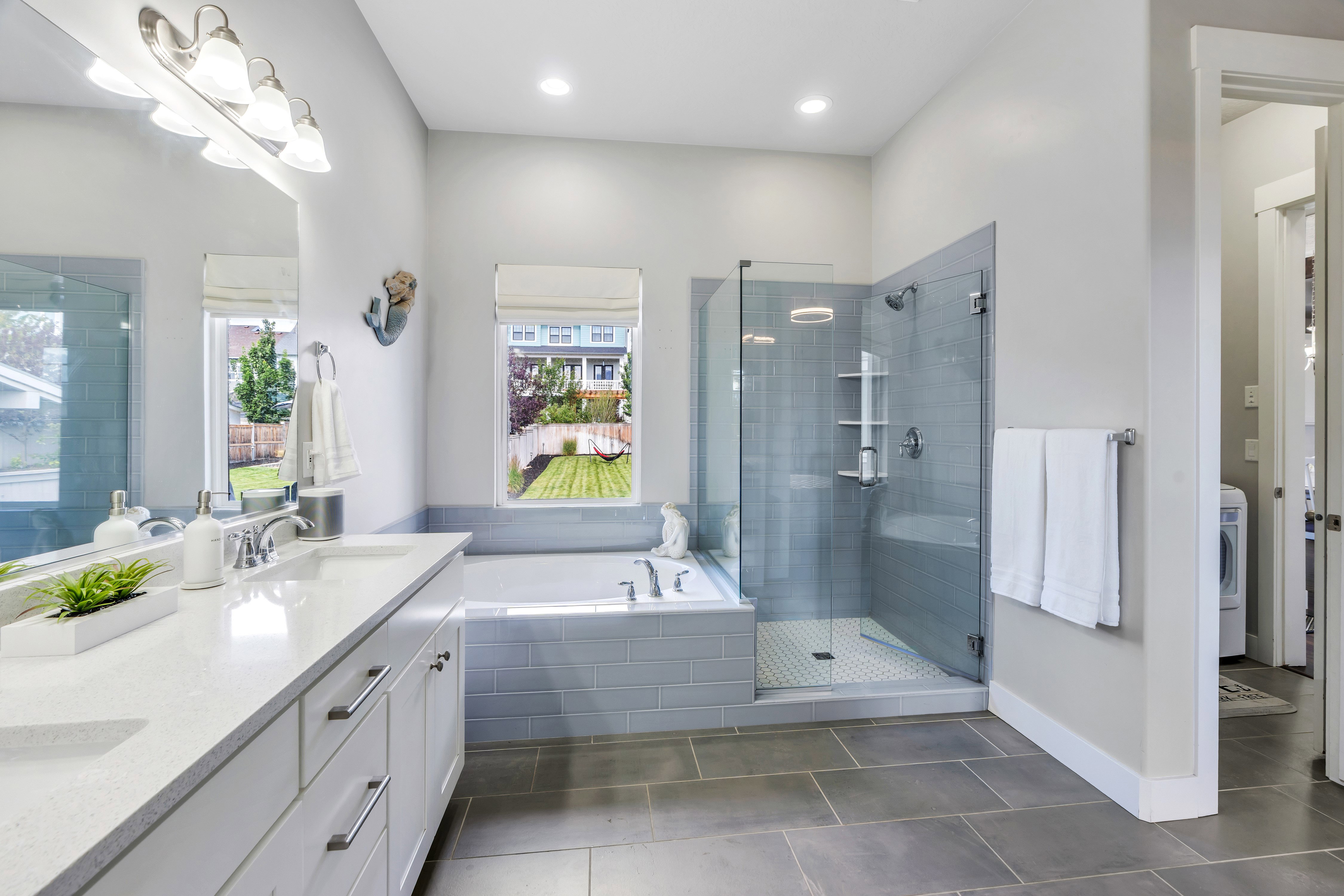 Bathroom featuring a large vanity with a single sink, an undermount tub with subway tile surround, a glass-enclosed shower with a bench and built-in shelving, and large format floor tiling