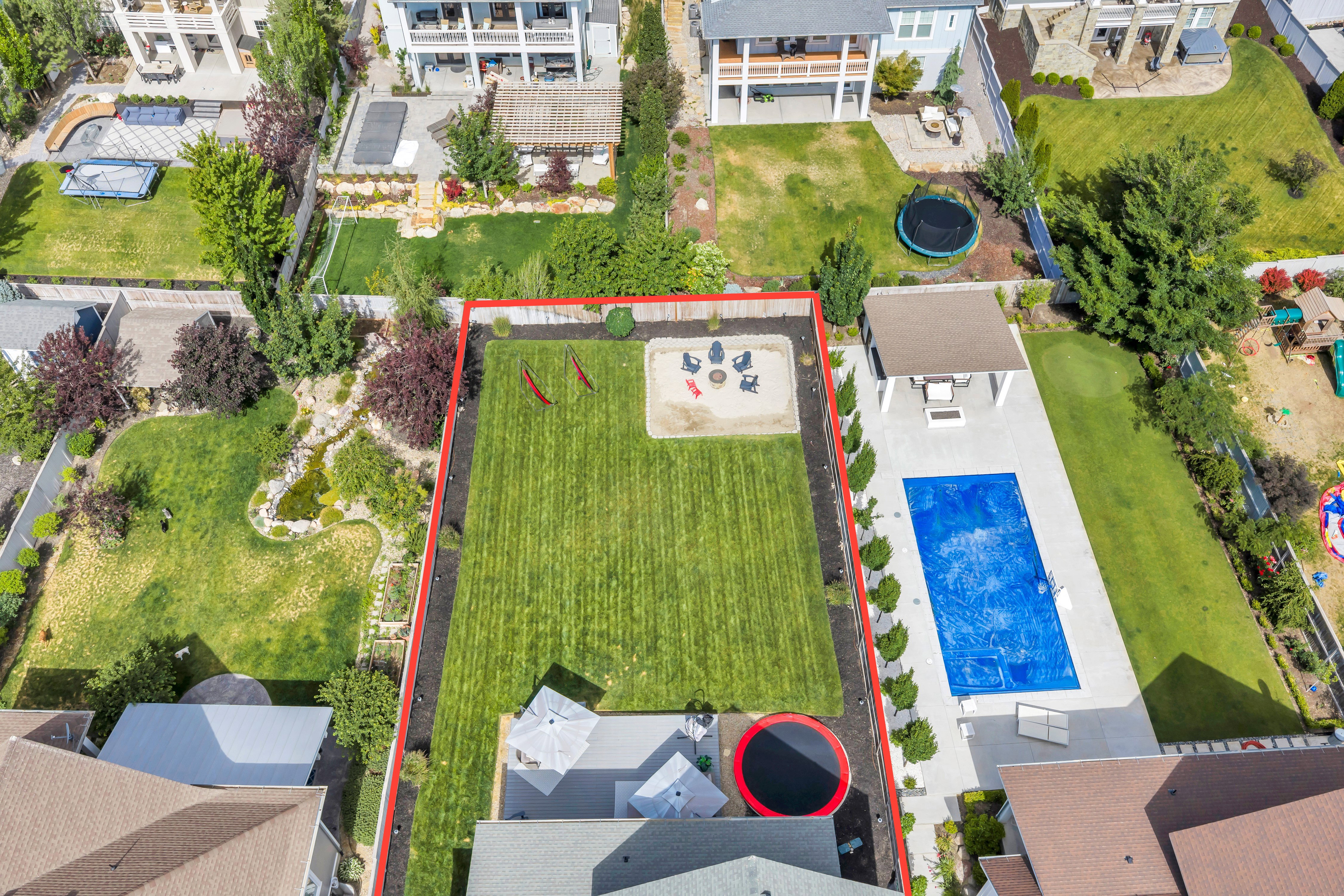 Expansive backyard featuring a large swimming pool, covered patio, fire pit area, and a substantial lawn