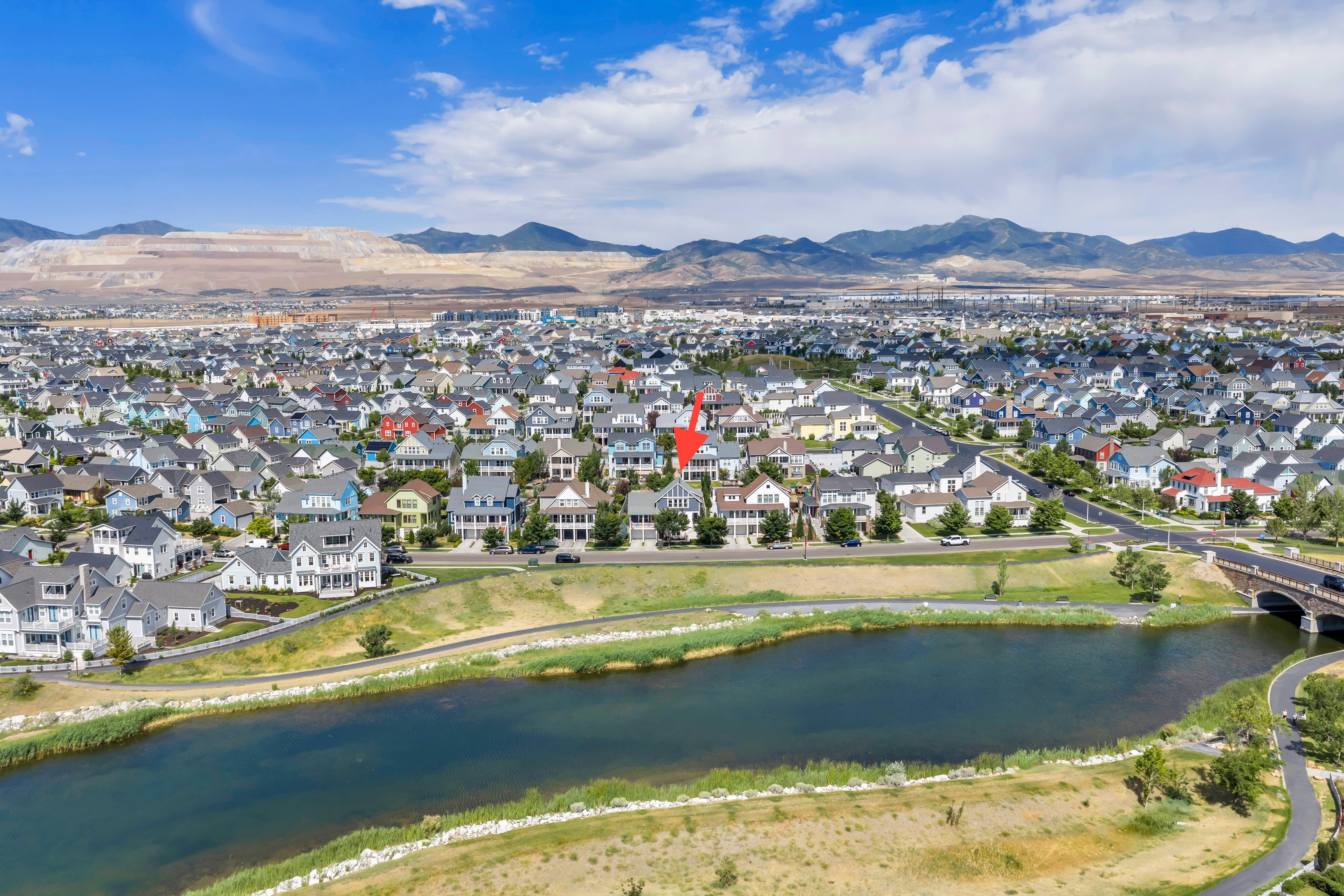 Aerial perspective showcasing a residential community with a large body of water in the foreground, bordered by a paved pathway and a bridge