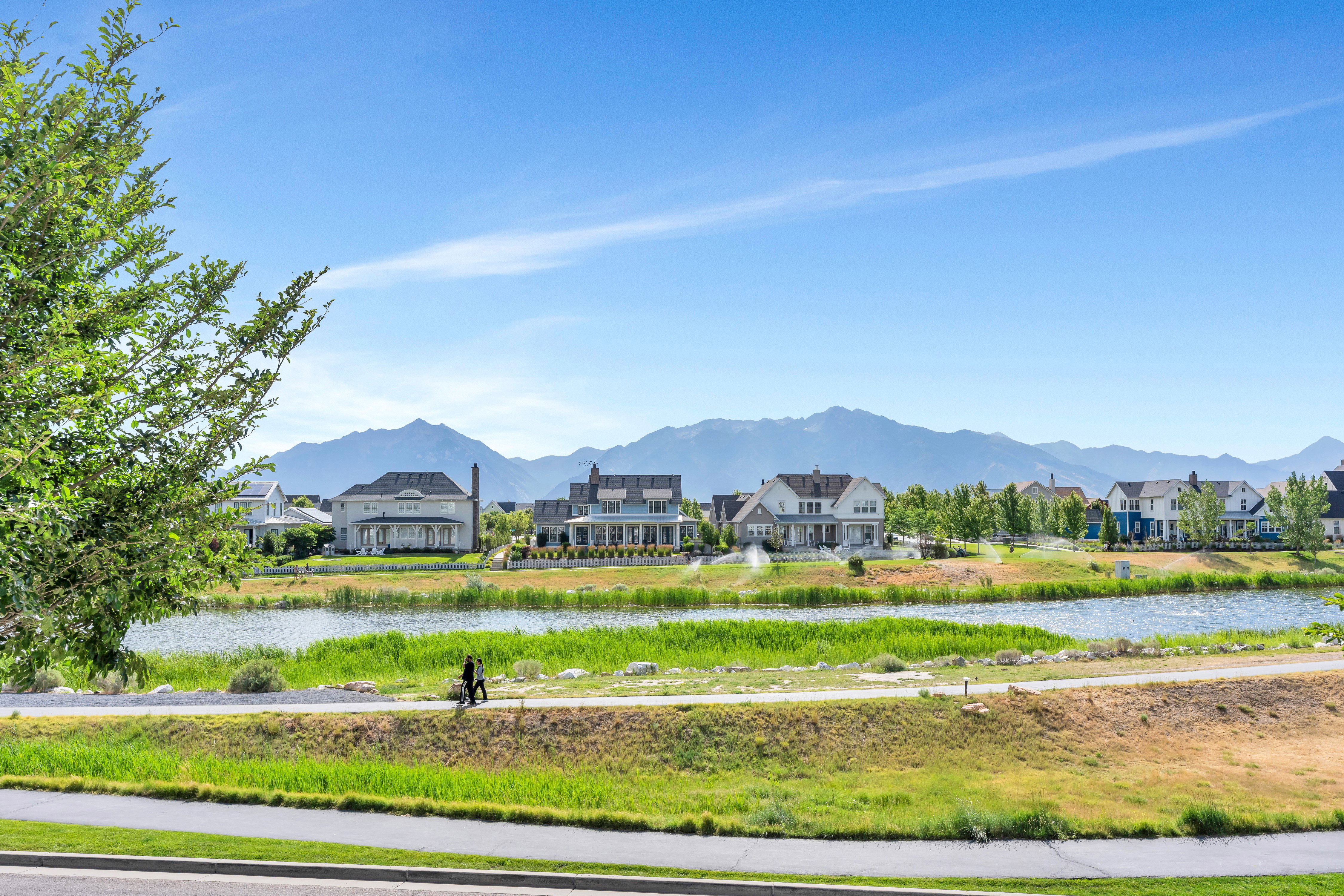 Scenic waterfront community featuring a paved pathway, expansive green spaces, and mountain backdrops