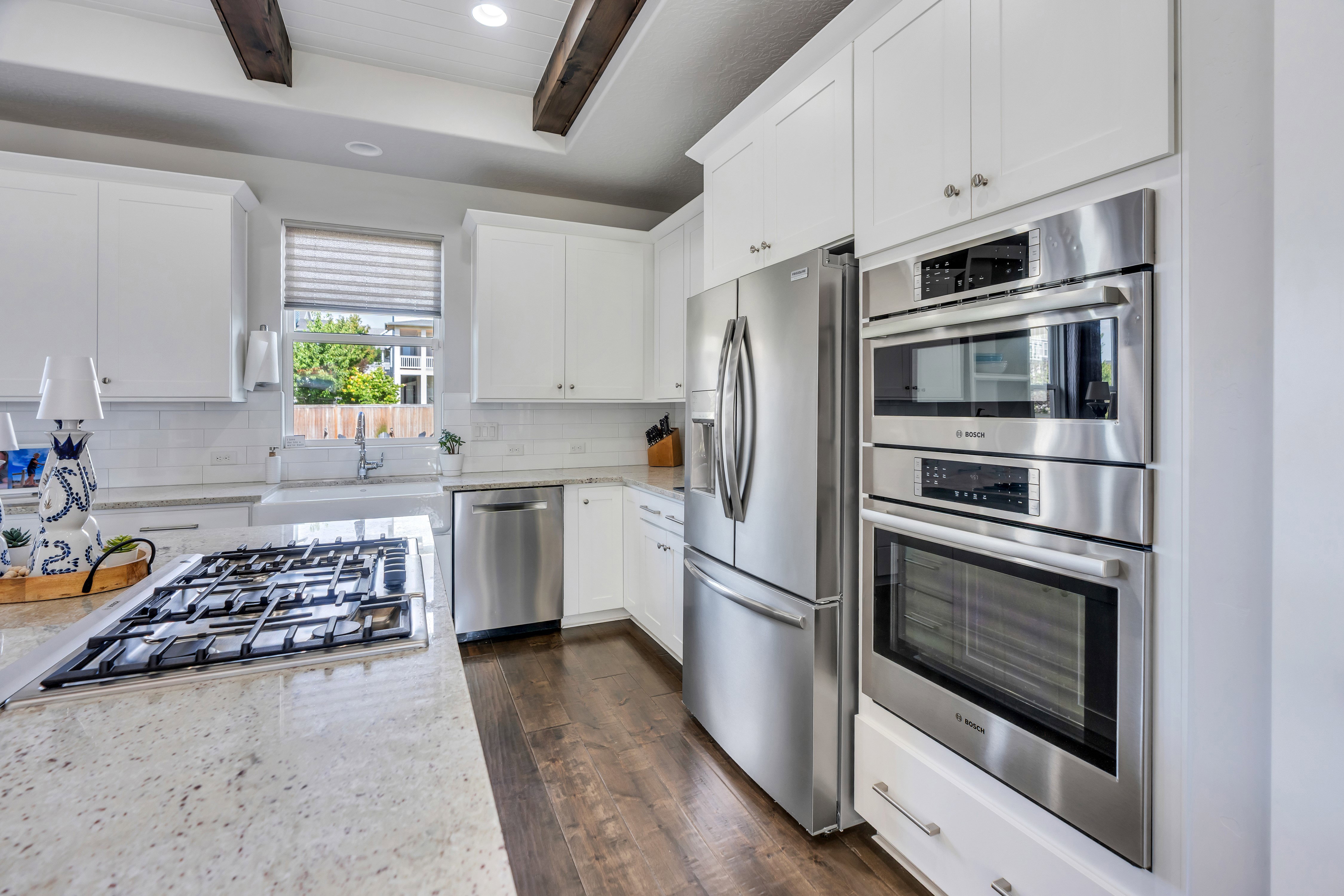 Gourmet kitchen featuring a built-in gas range, white cabinetry, integrated stainless steel appliances, granite countertops, and wood-finish flooring