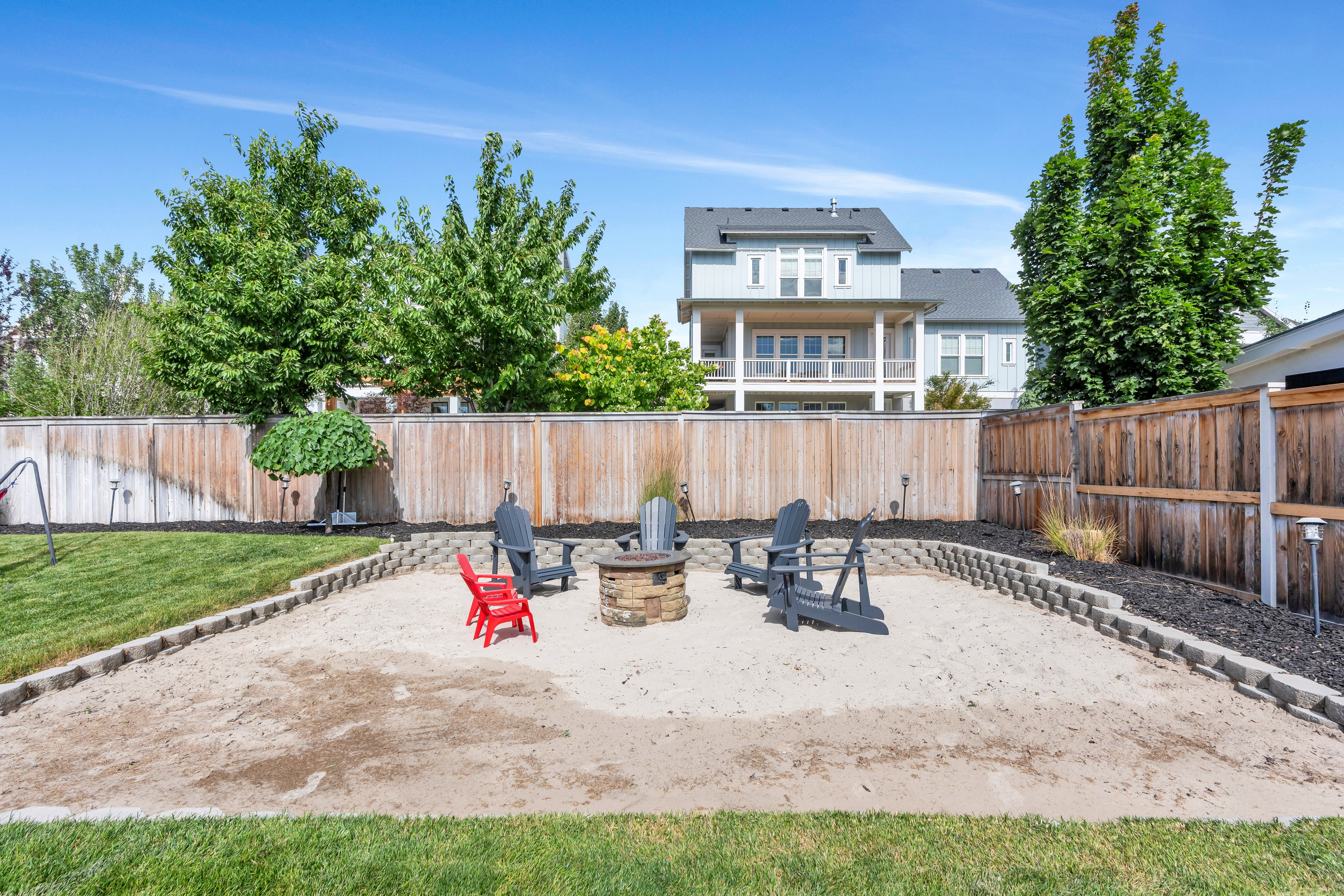 Outdoor gathering space featuring a sand-filled area, a stone-clad fire pit, and a retaining wall