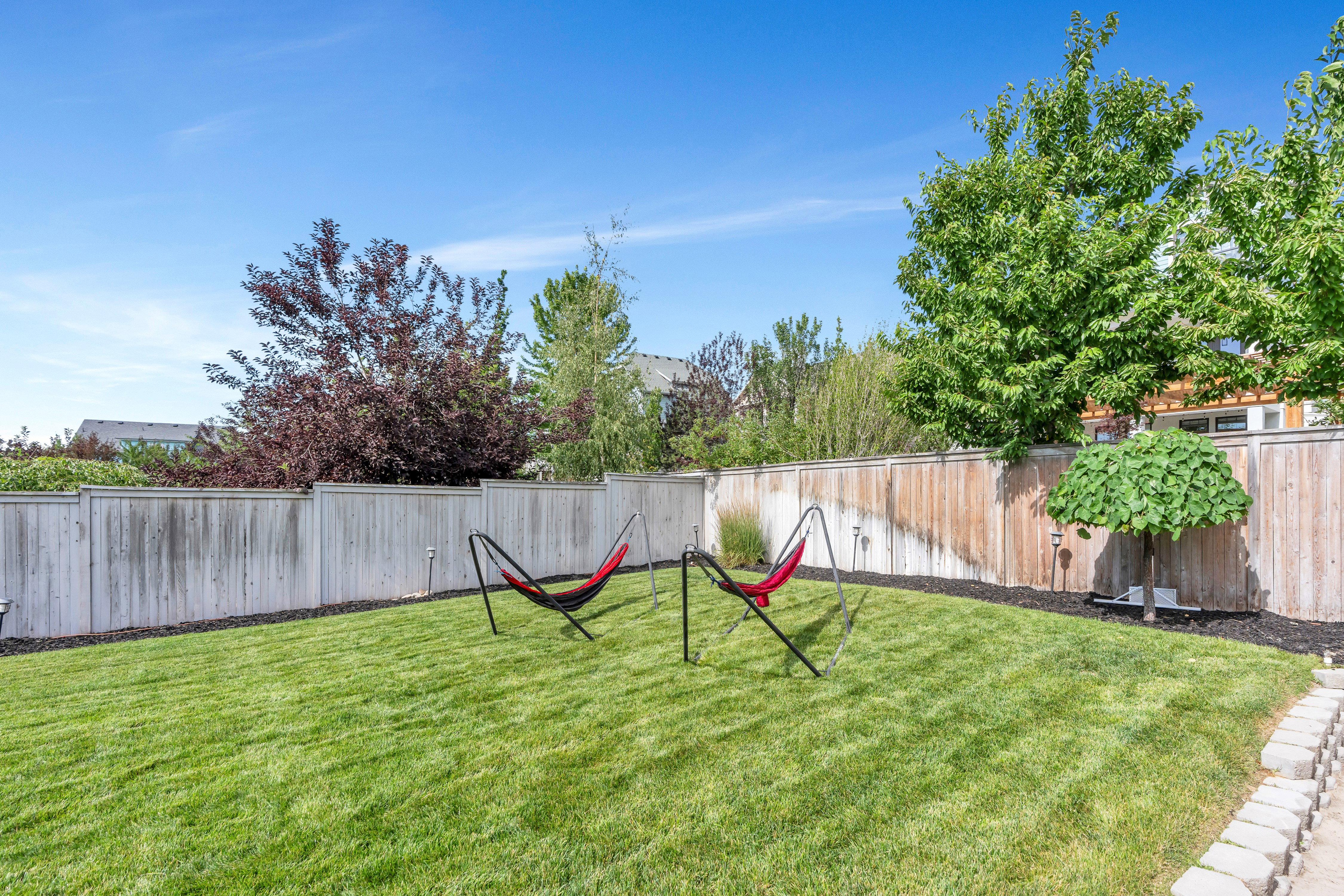 Expansive lawn area featuring a wooden privacy fence, mature trees, and landscaping beds with dark ground cover