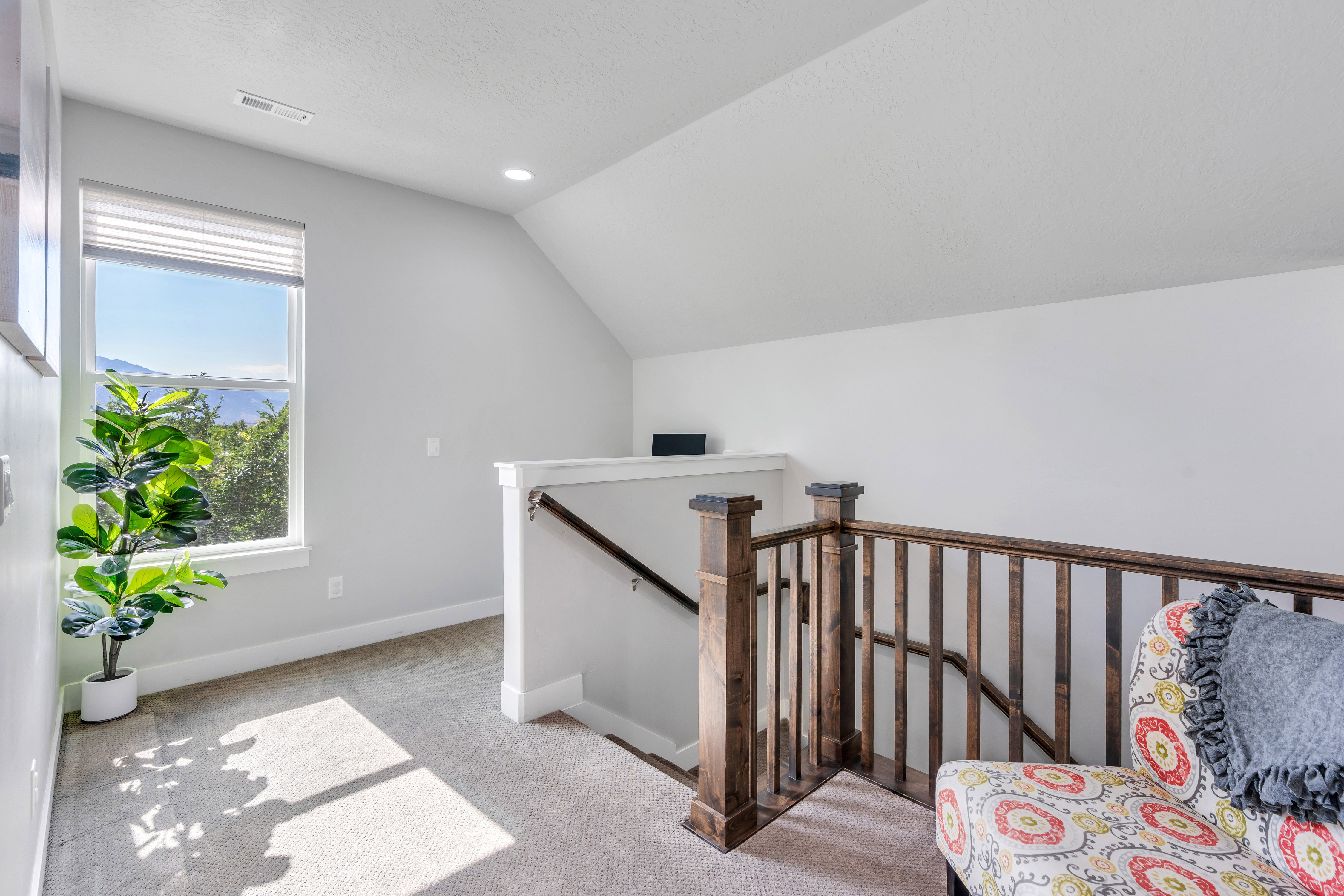 Carpeted landing with a large window, white walls, and a wooden staircase railing