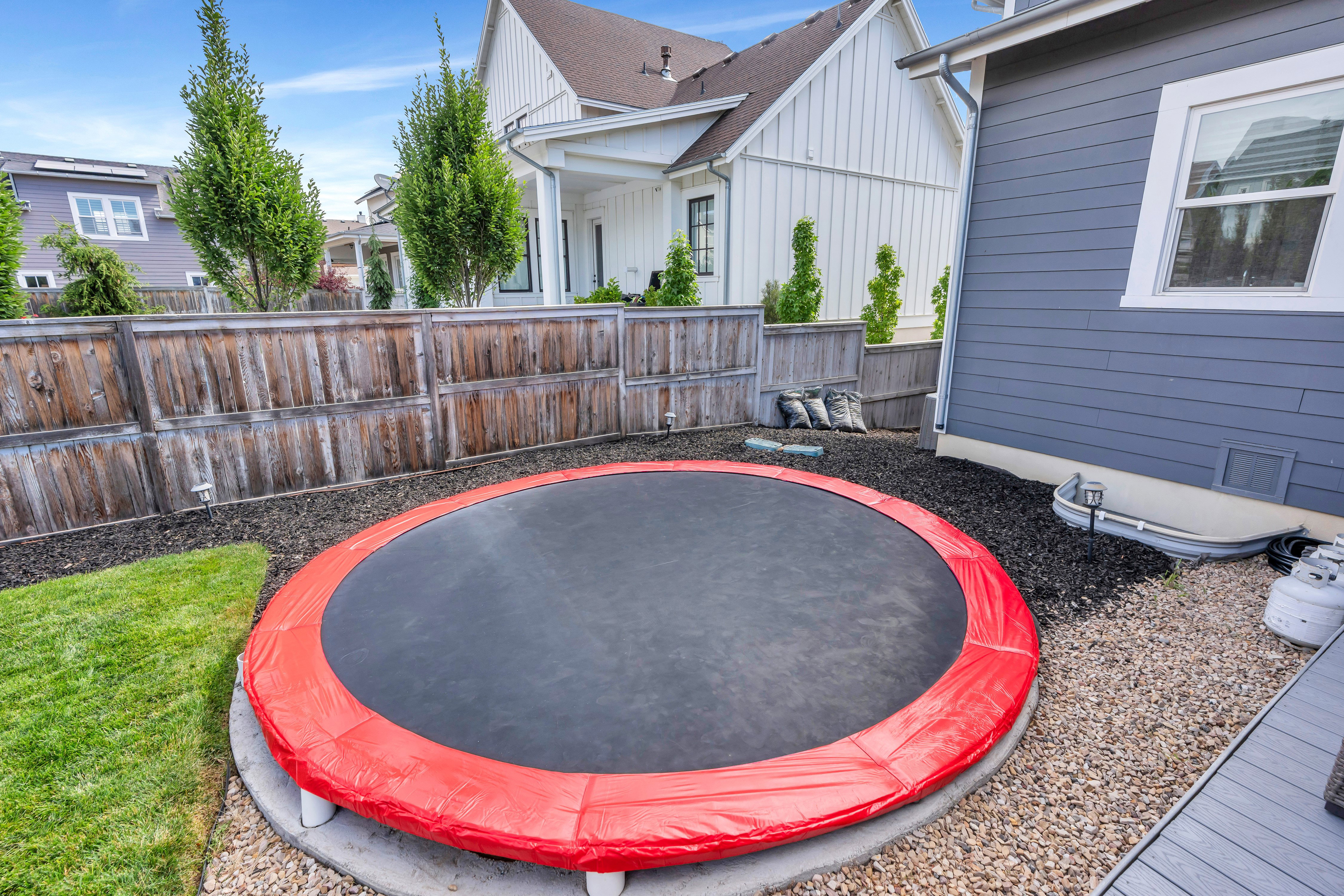 In-ground trampoline with a red safety pad, surrounded by a concrete ring and gravel