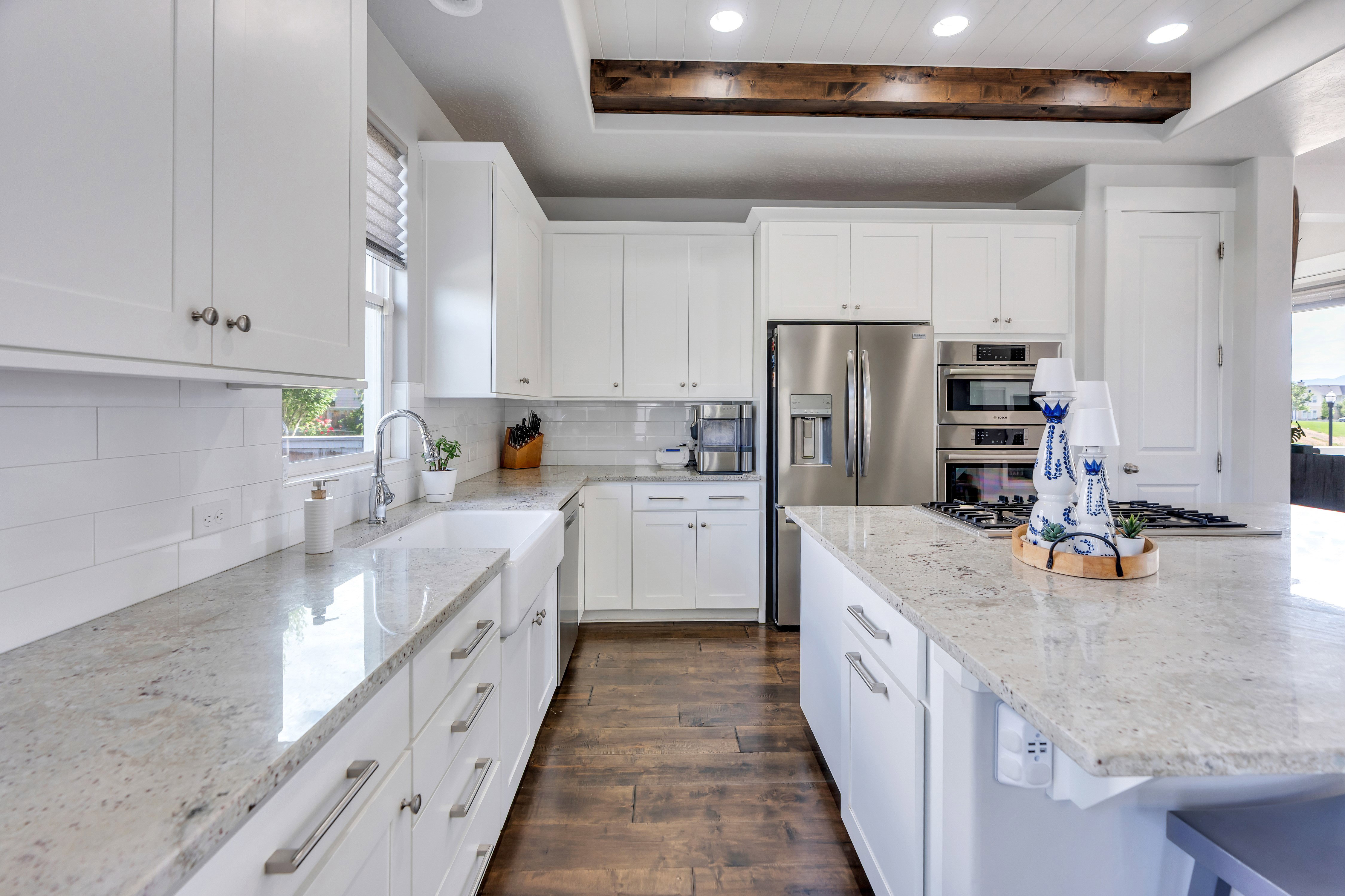 Gourmet kitchen featuring white shaker cabinetry, light-toned granite countertops, wood-finish flooring, stainless steel appliances, and a built-in oven