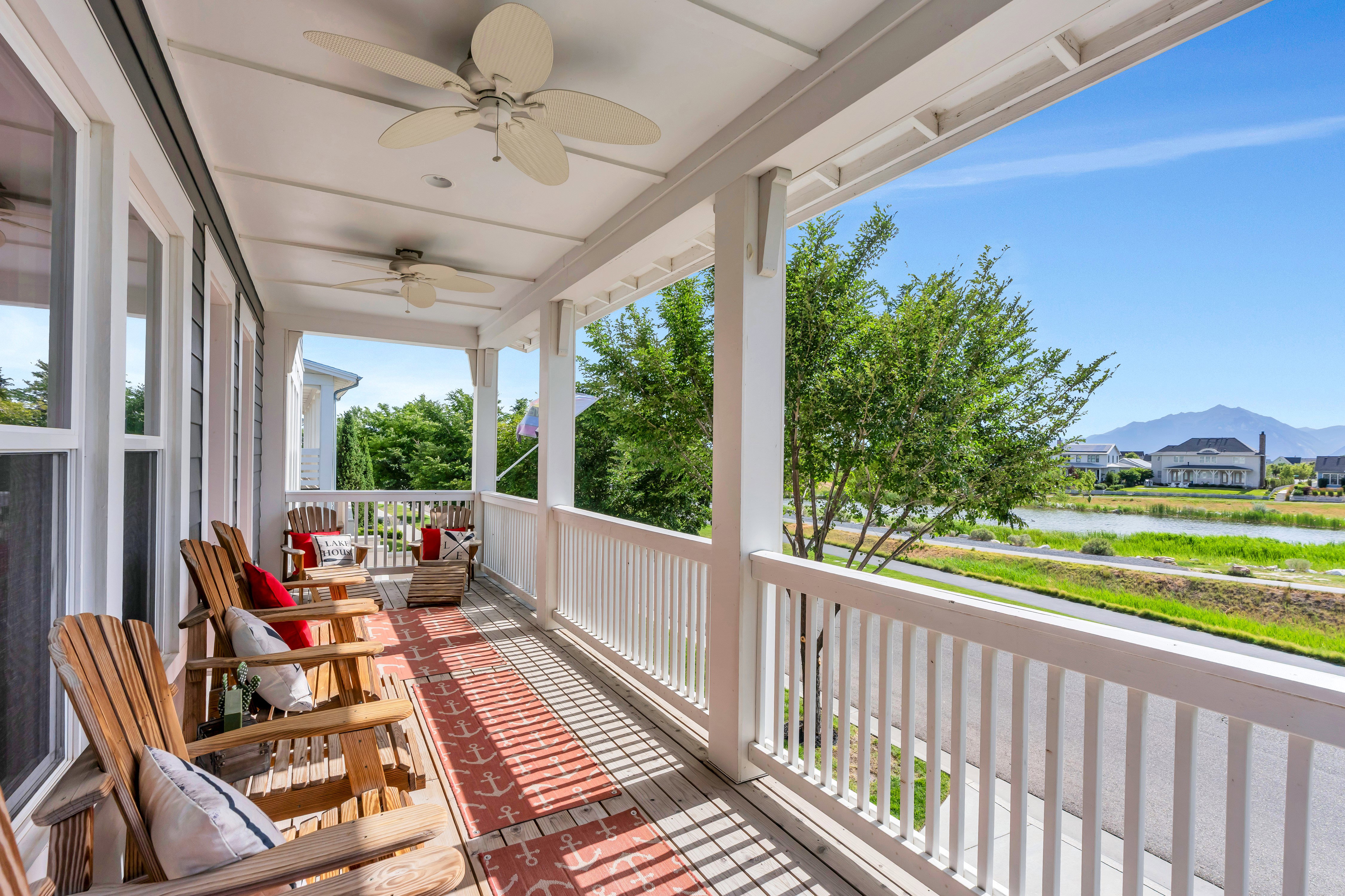 Expansive covered front porch featuring two ceiling fans, white columns and railings, wood-finish flooring, and ample natural light