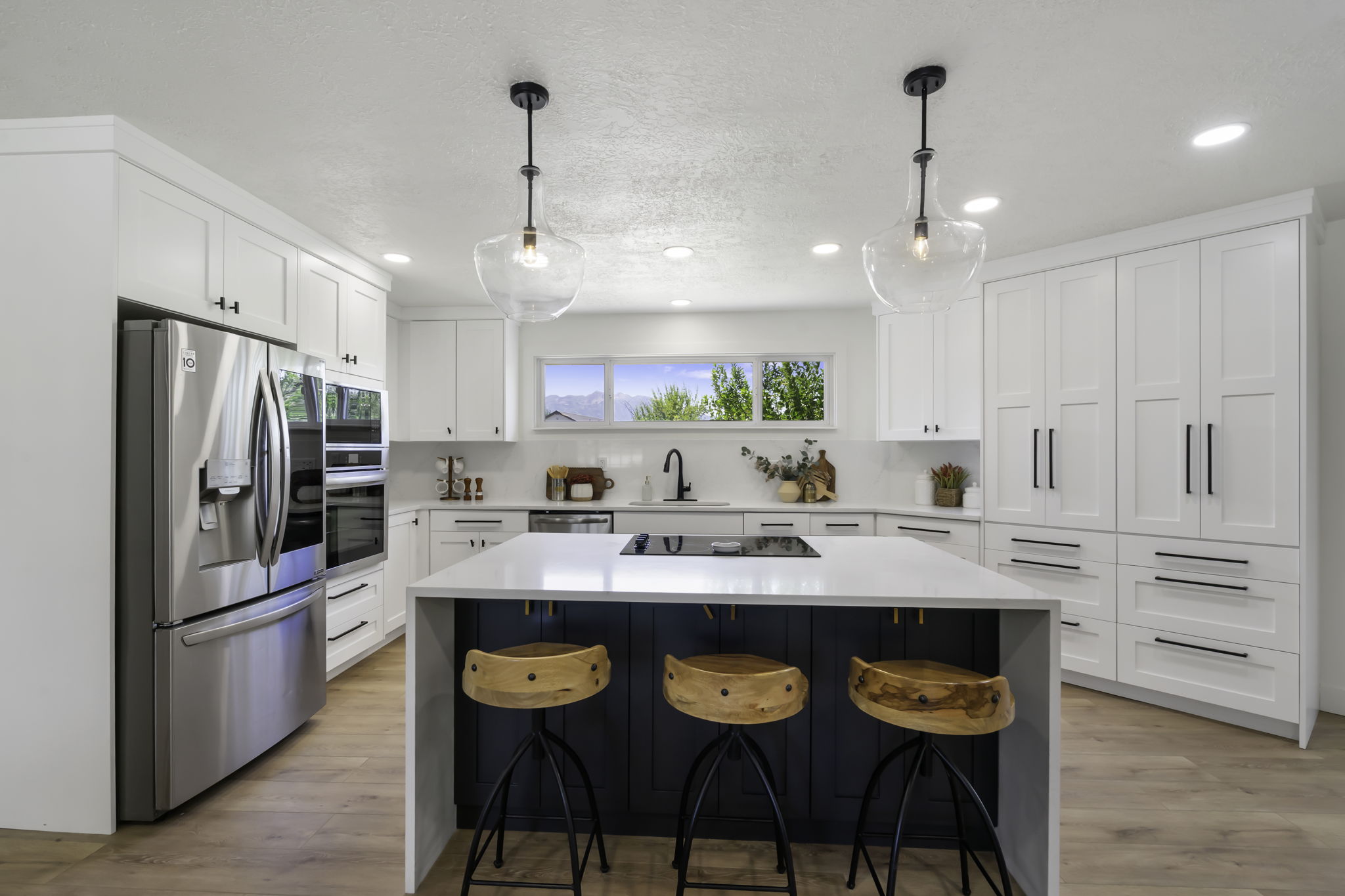 Kitchen featuring white cabinetry, a large center island with seating, stainless steel appliances, wood-finish flooring, and pendant lighting
