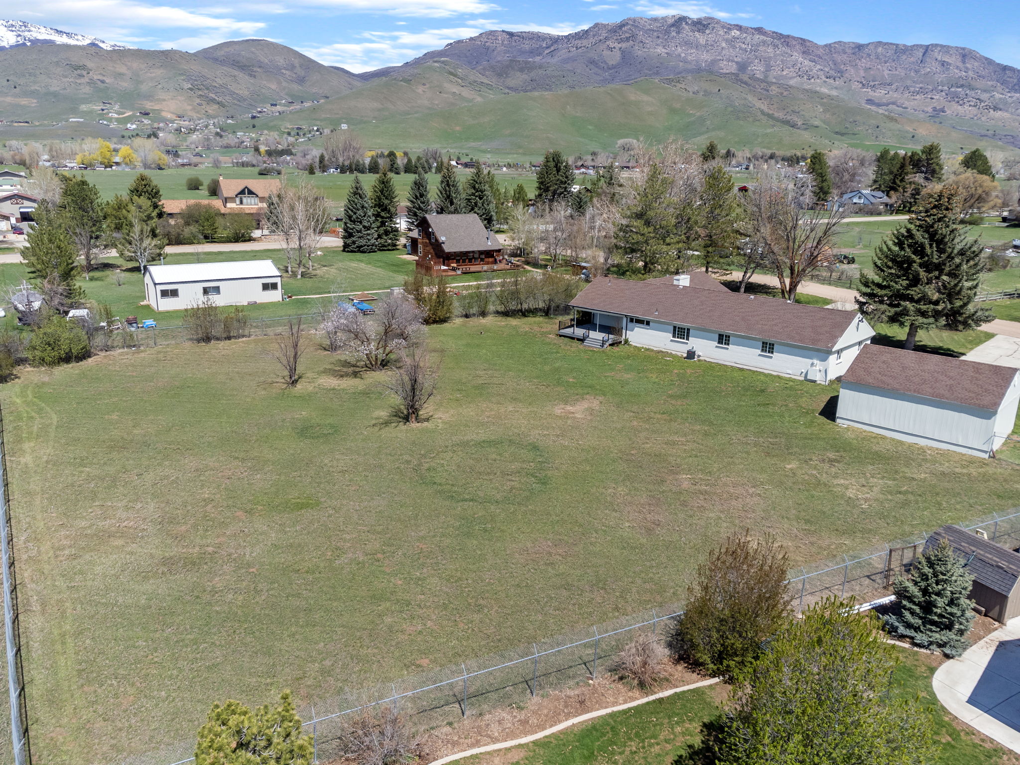Expansive green lot featuring a single-story residence, a detached garage, and a separate outbuilding, all set against a backdrop of distant mountains