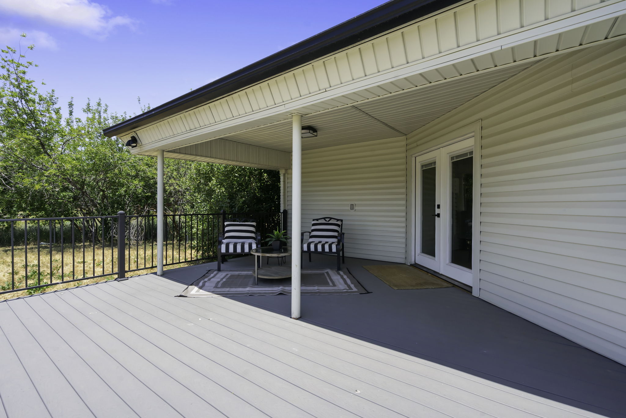 Expansive composite deck featuring a covered patio, dual ceiling-mounted light fixtures, white vinyl siding, and double glass-paneled exterior doors