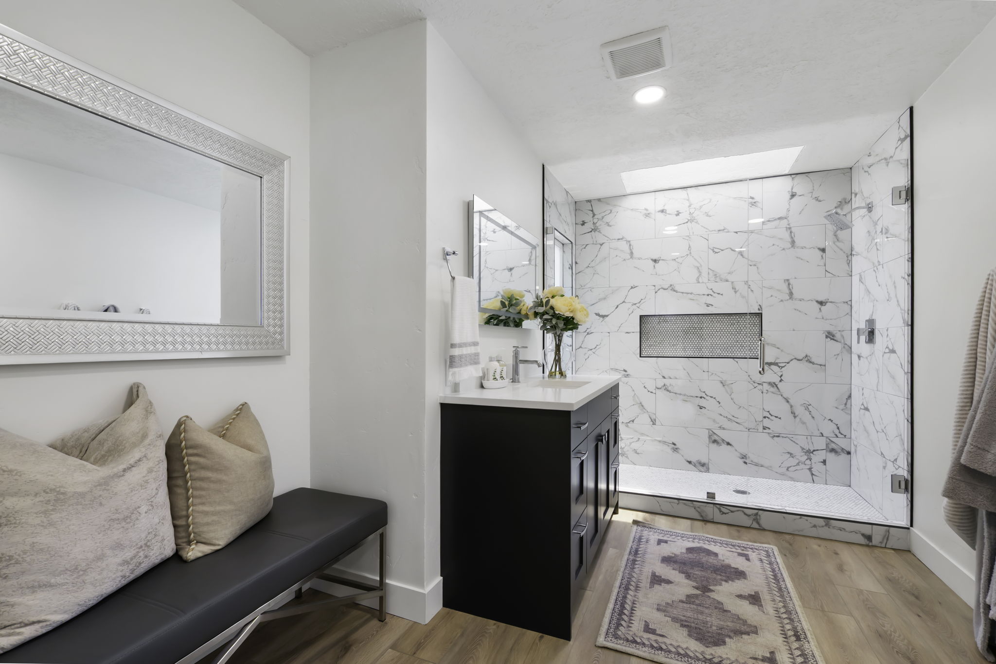 Spacious bathroom featuring a frameless glass shower enclosure with marble-finish tile, an integrated shower niche, and a contrasting dark wood-finish vanity with a light-toned countertop