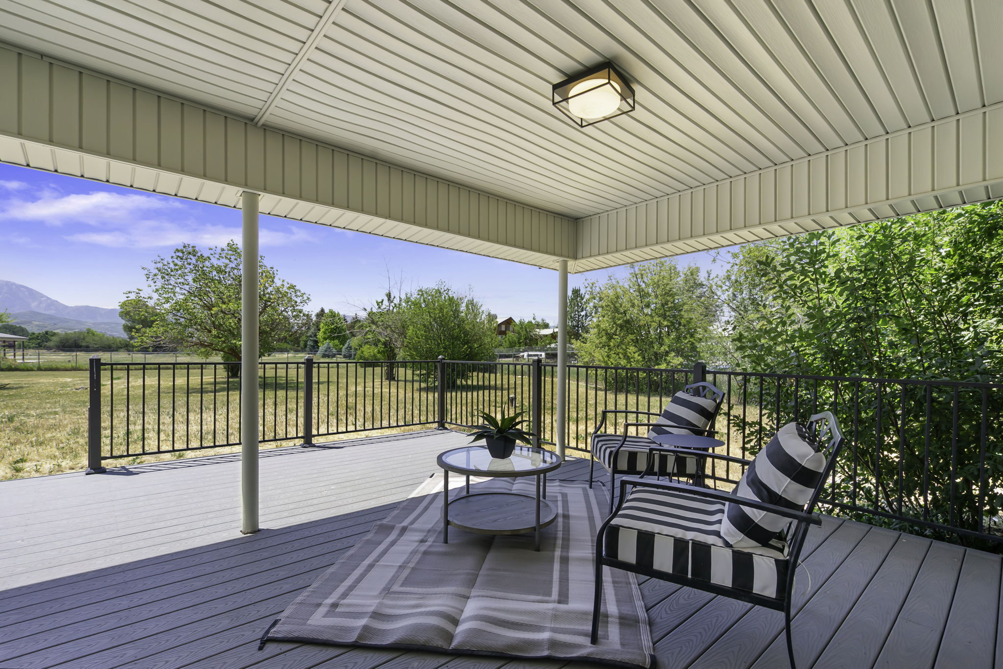 Covered patio featuring a slatted ceiling, recessed lighting, composite decking, and metal railings overlooking natural scenery