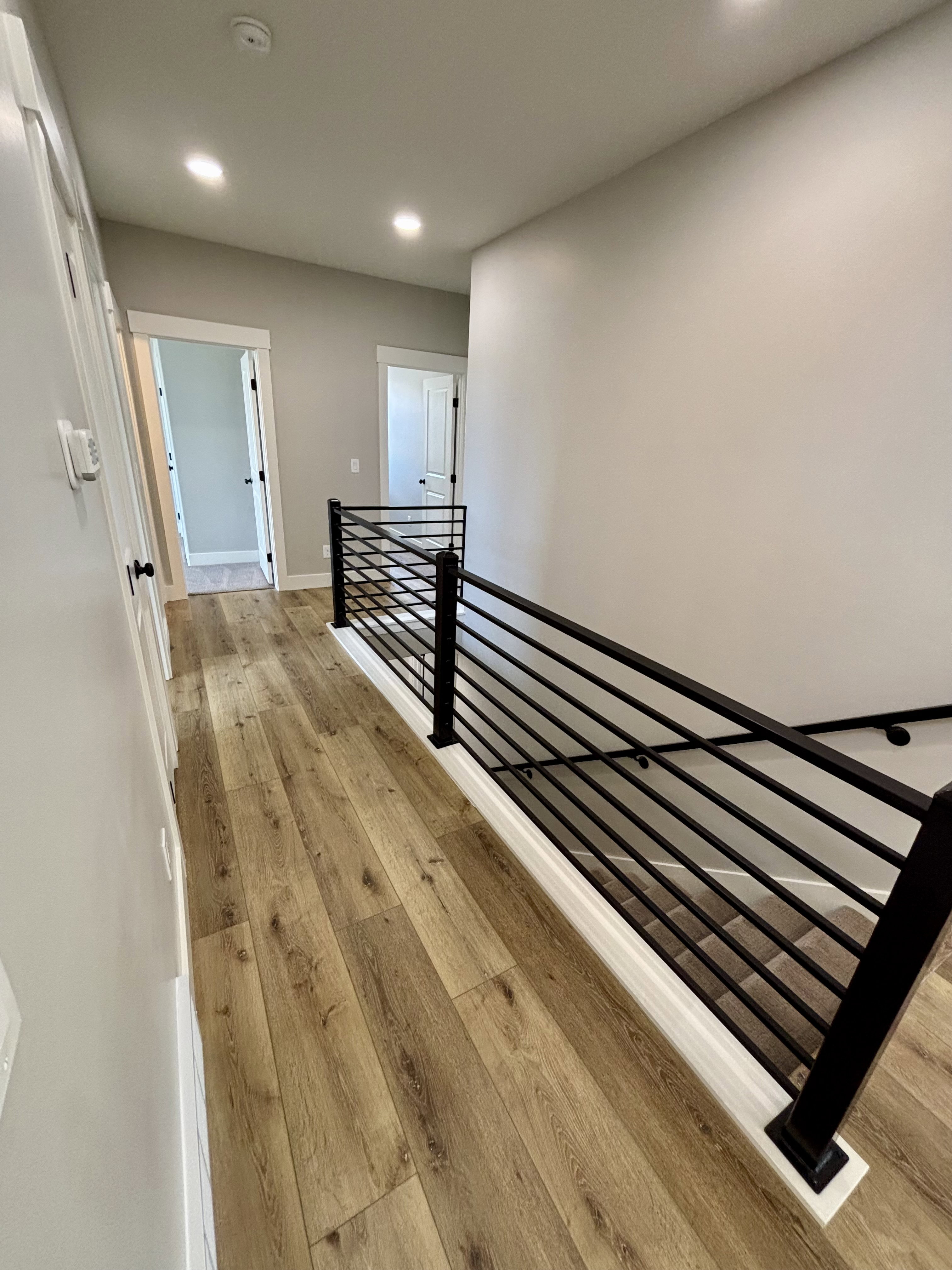 Hallway featuring lap wood style flooring, recessed lighting, and a contemporary black metal baluster railing