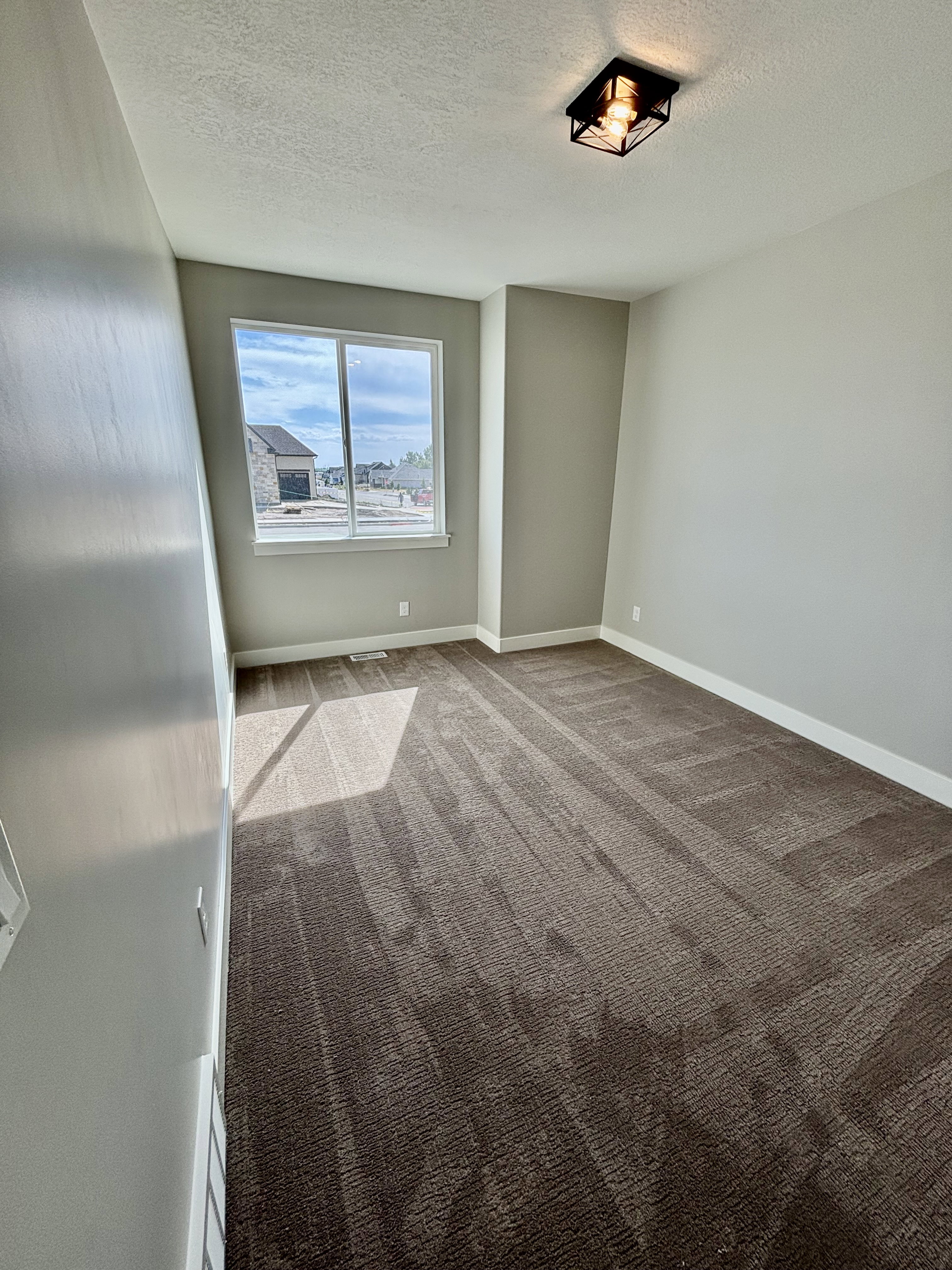 Light-filled room featuring a large window, neutral wall paint, patterned carpet flooring, and a contemporary ceiling light fixture