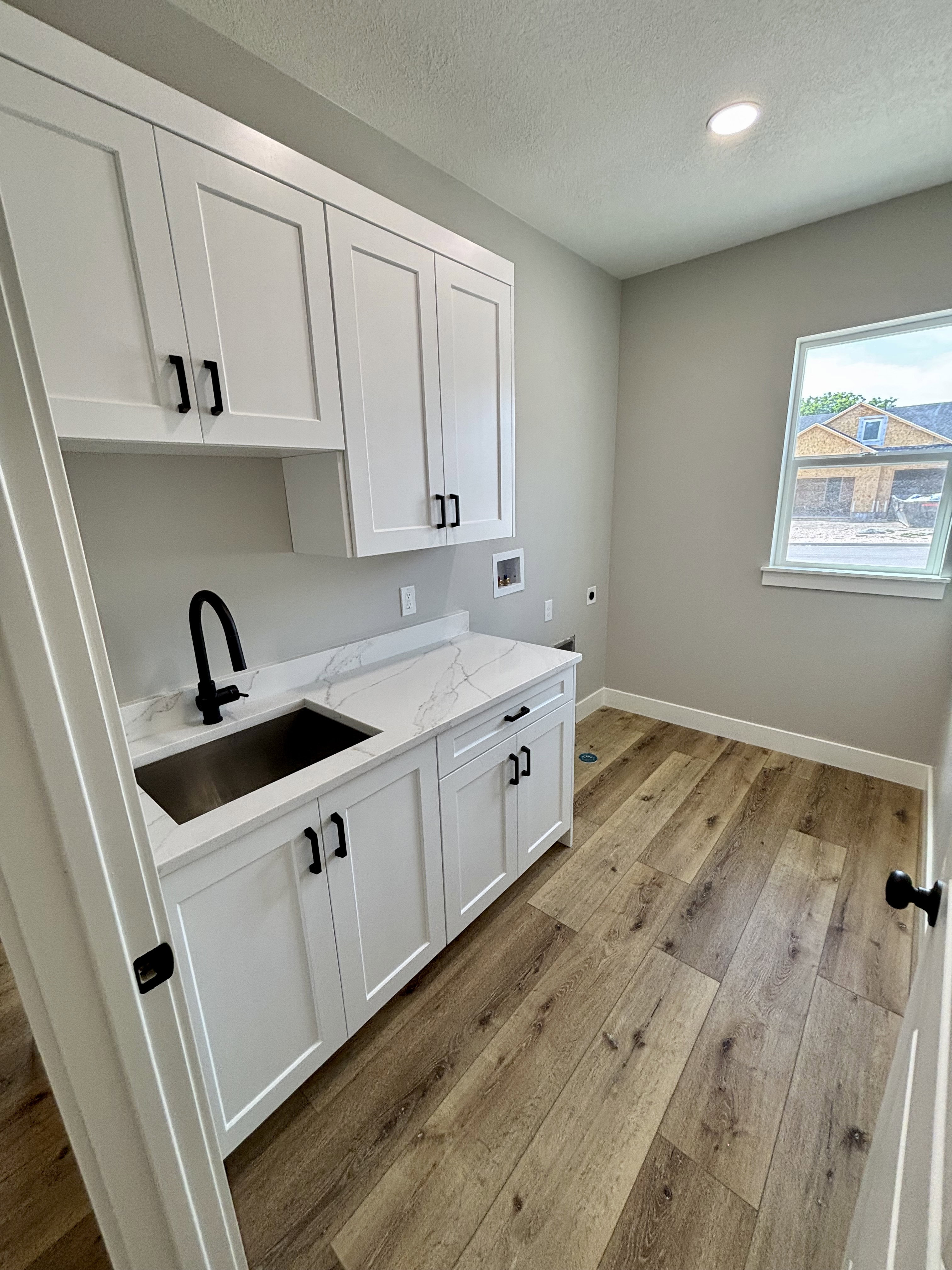 Laundry area featuring white shaker-style cabinetry, a stainless steel undermount sink with a matte black faucet, and a white quartz countertop with subtle gray veining