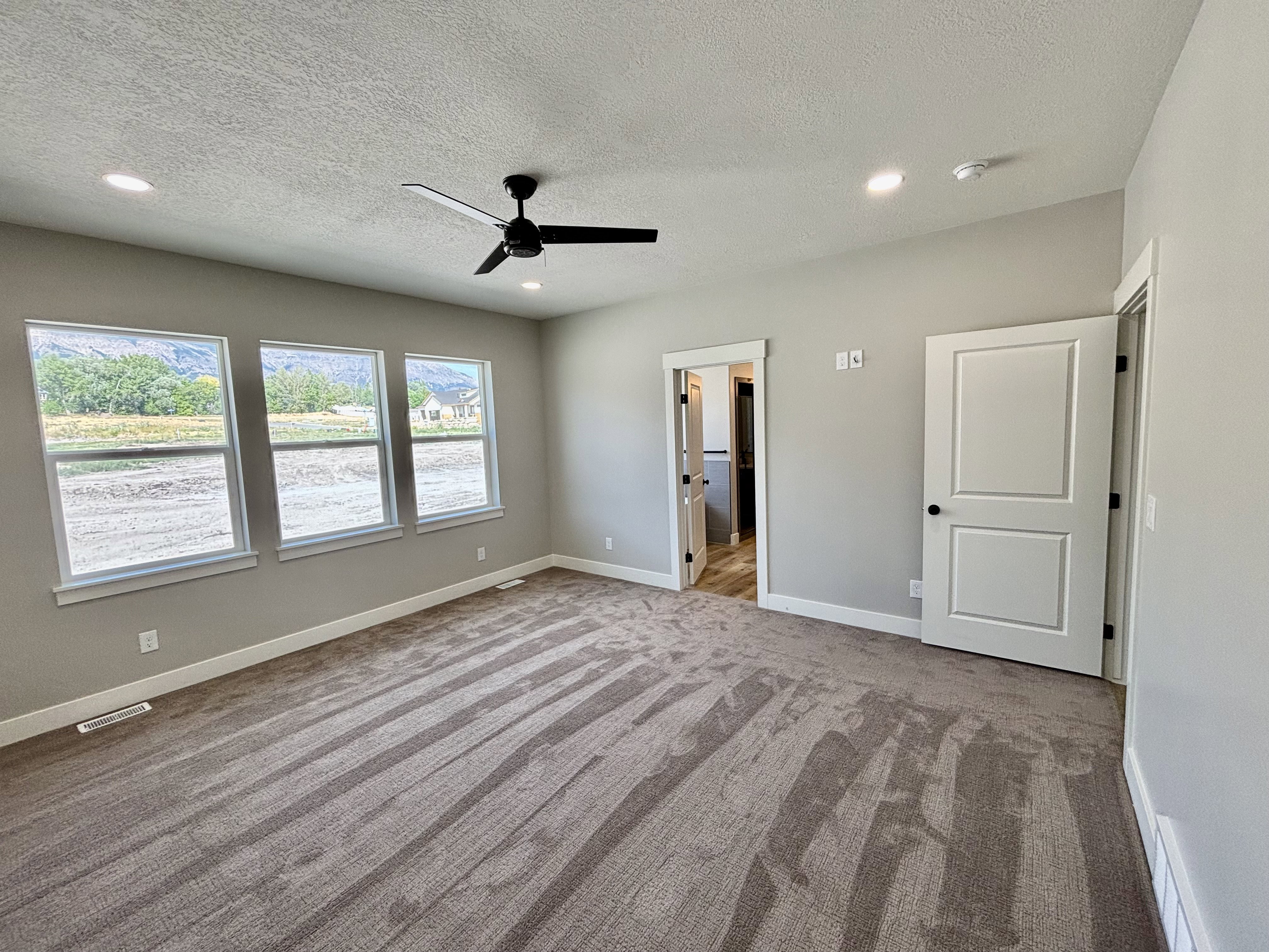 Master bedroom featuring three large windows, plush carpeting, a contemporary ceiling fan, and recessed lighting