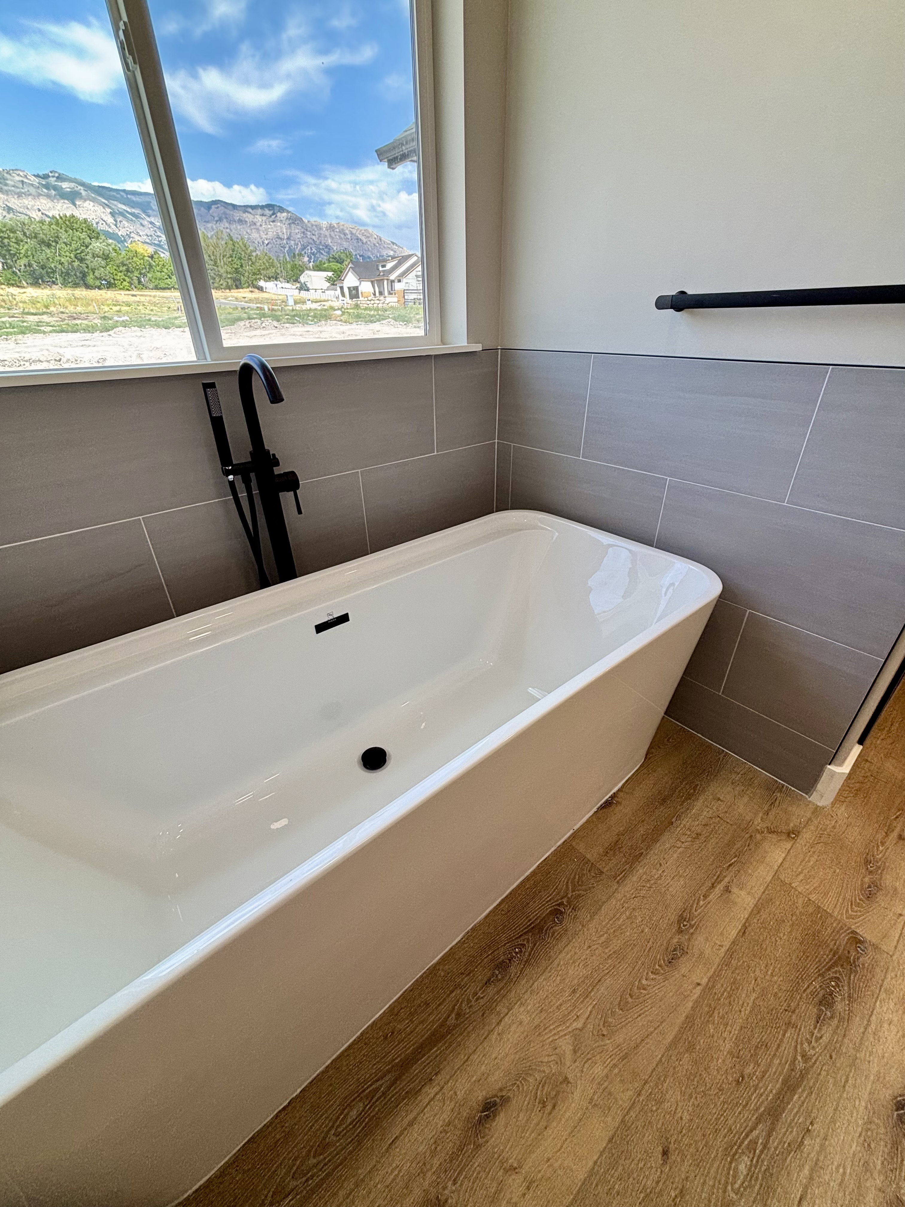 Freestanding soaking tub with a matte black floor-mounted faucet, set against a tiled accent wall and lvp wood style flooring