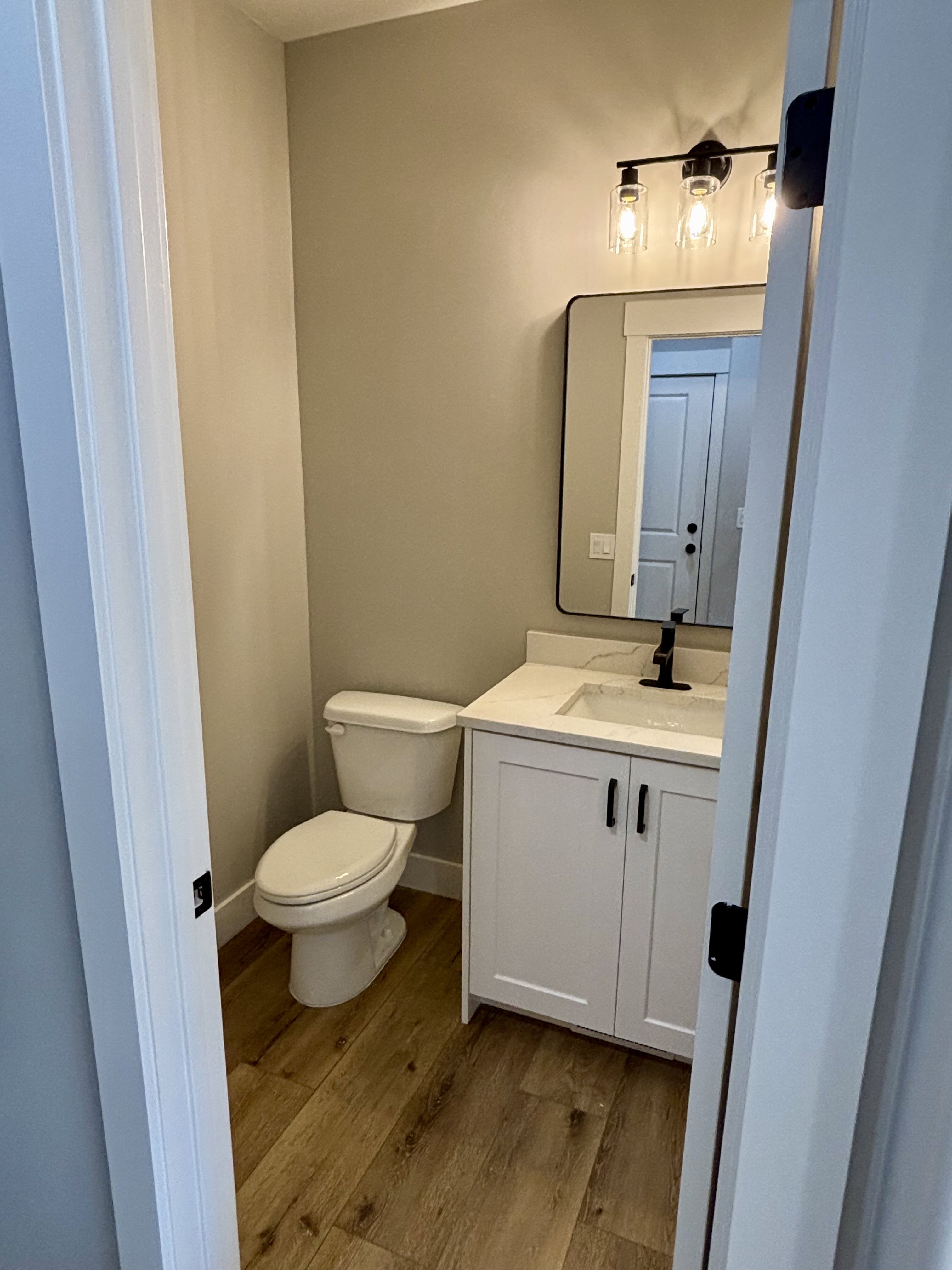 Contemporary bathroom featuring a white vanity with shaker-style cabinetry, a quartz countertop with an integrated sink, and lvp wood  style flooring