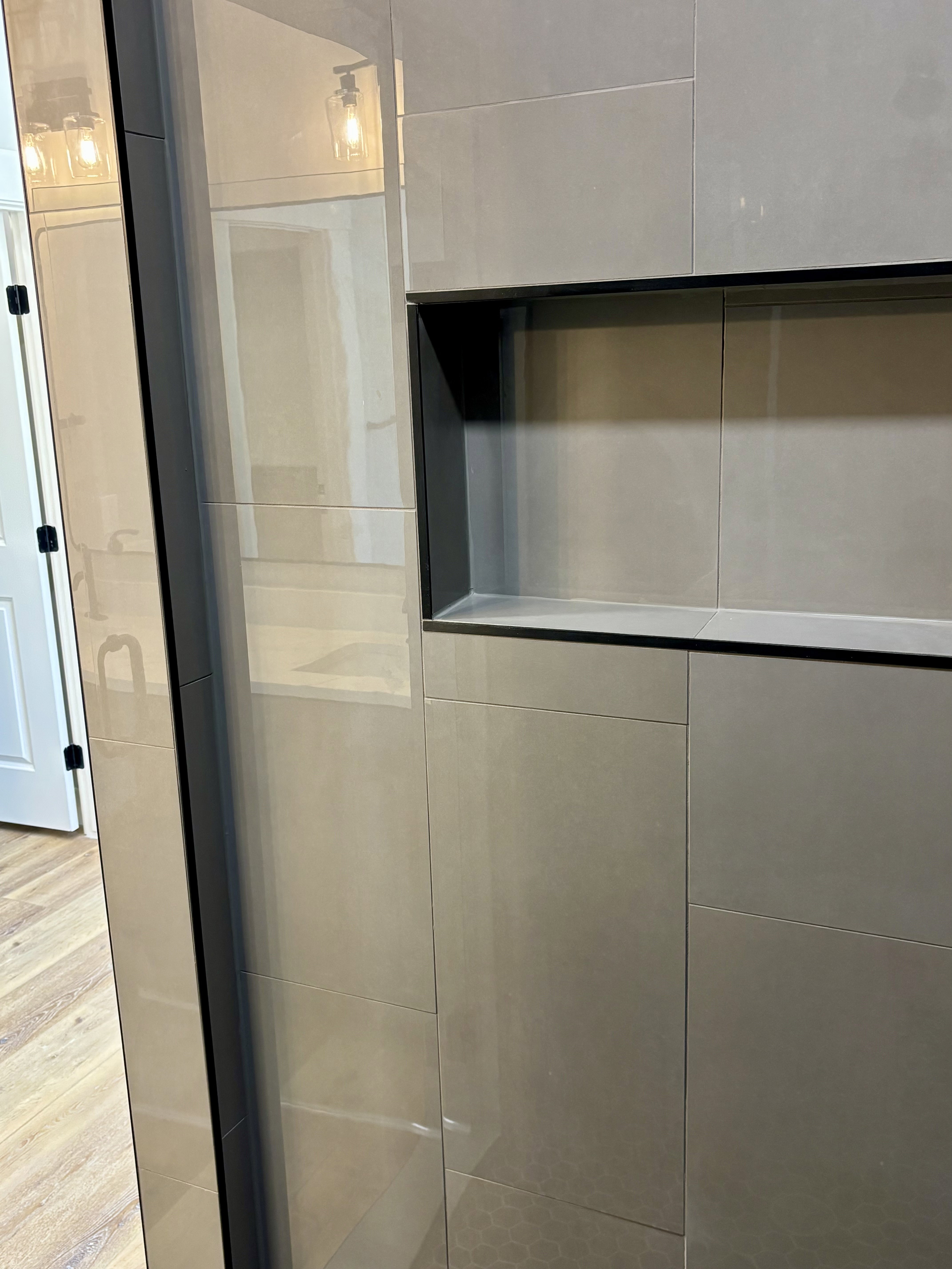 Shower enclosure featuring large format light gray tiles and a recessed black-framed niche