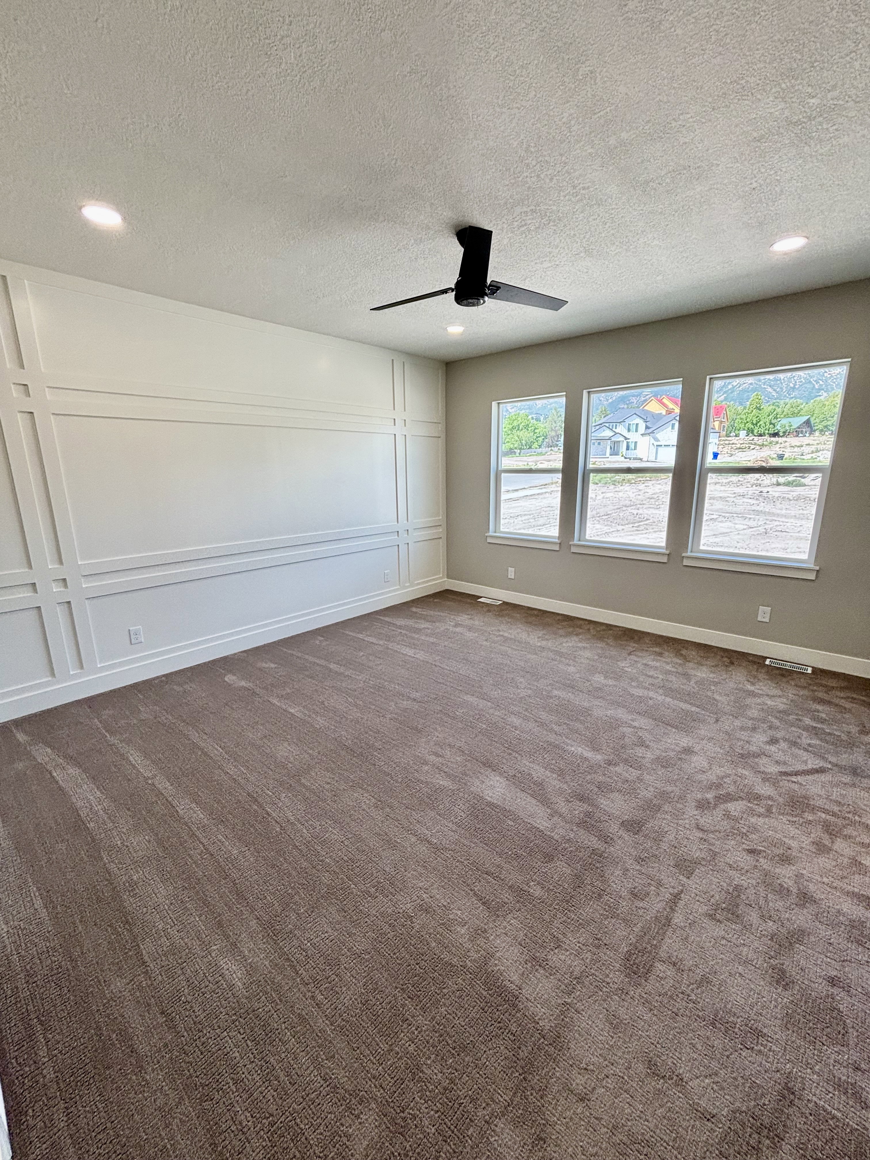 Master bedroom featuring broadloom carpet, an accent wall with decorative trim, and a modern black ceiling fan