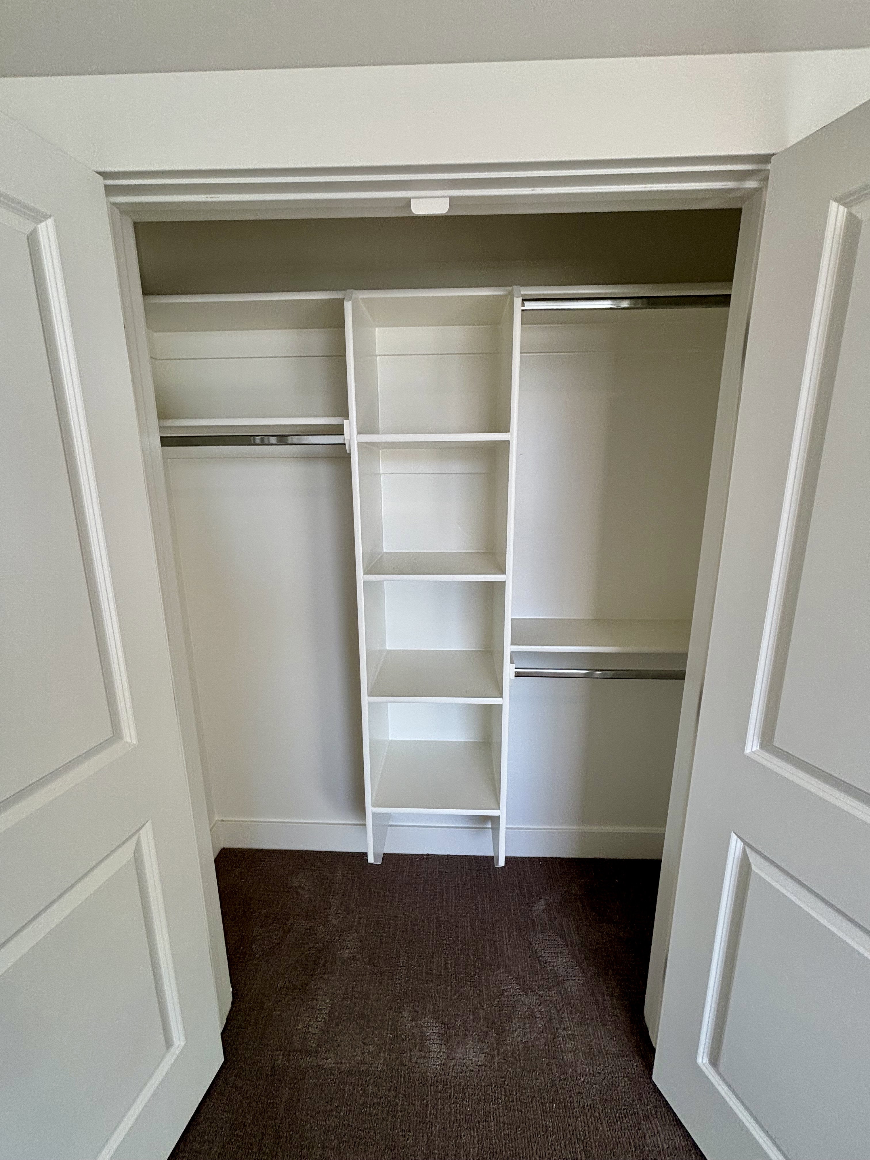 Spacious closet featuring white bi-fold doors, built-in shelving, and dual hanging rods over dark-hued carpet