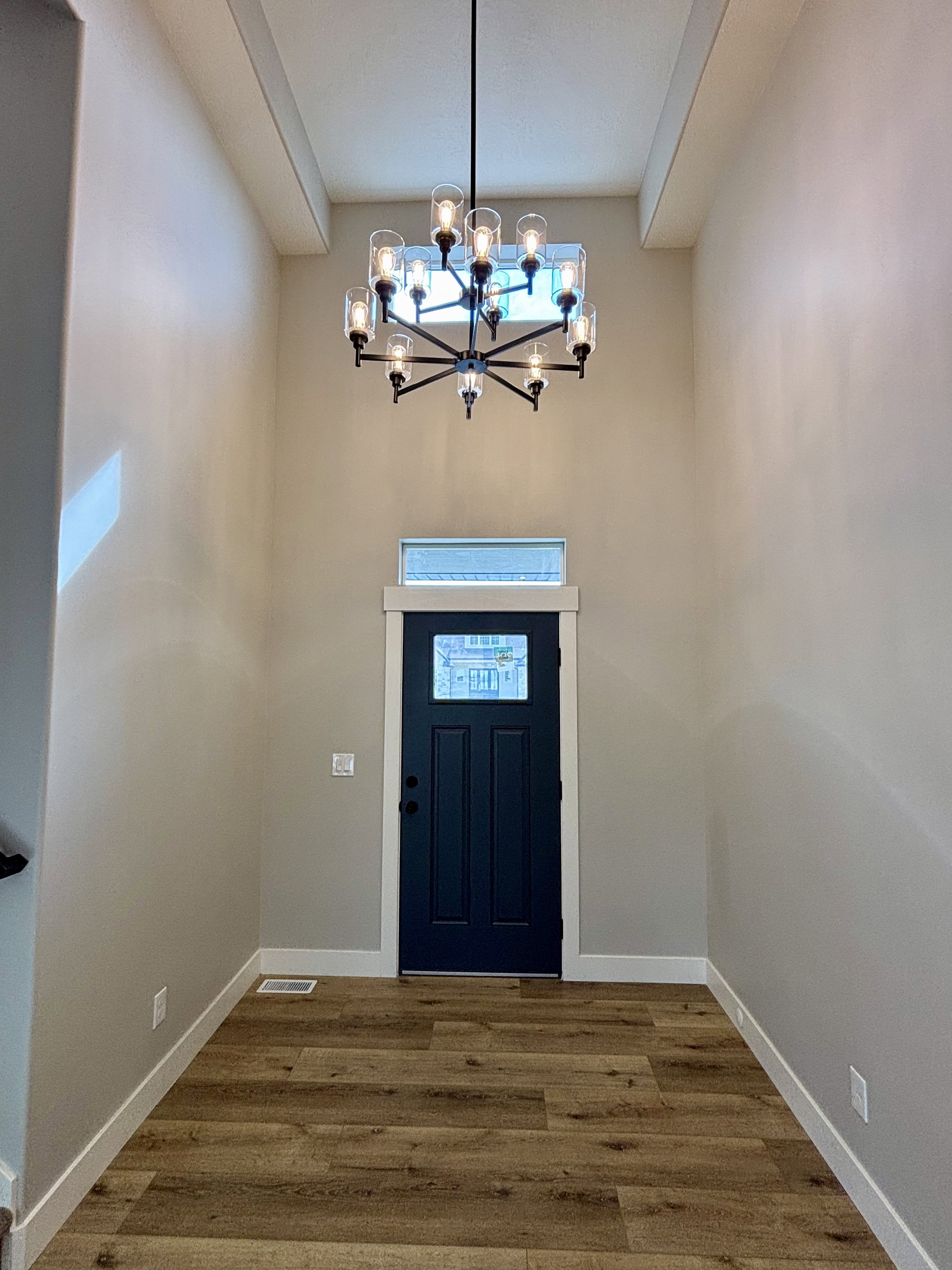 Two-story entry featuring wood-finish flooring, a dark blue paneled door with upper glass paneling, a transom window, and a twelve-light chandelier