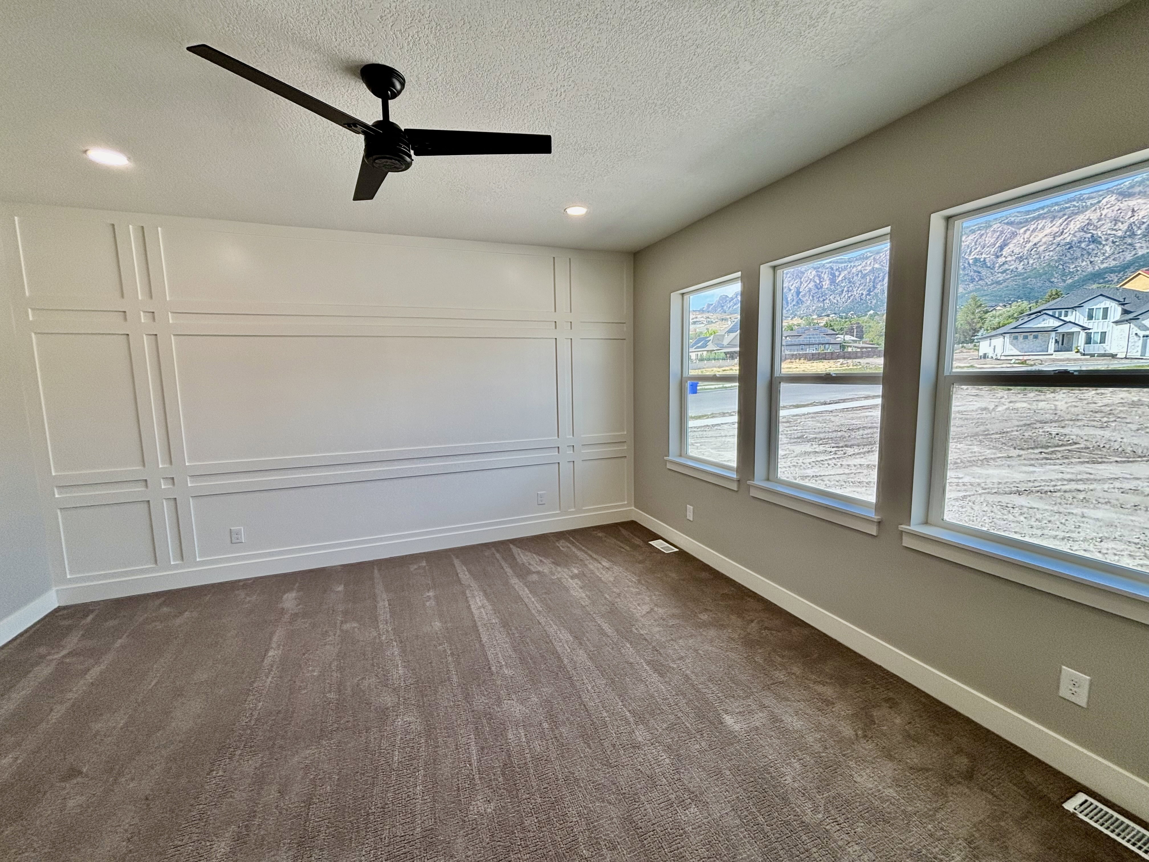 Master bedroom with accent wall featuring decorative molding, dark-toned ceiling fan, recessed lighting, and three tall windows