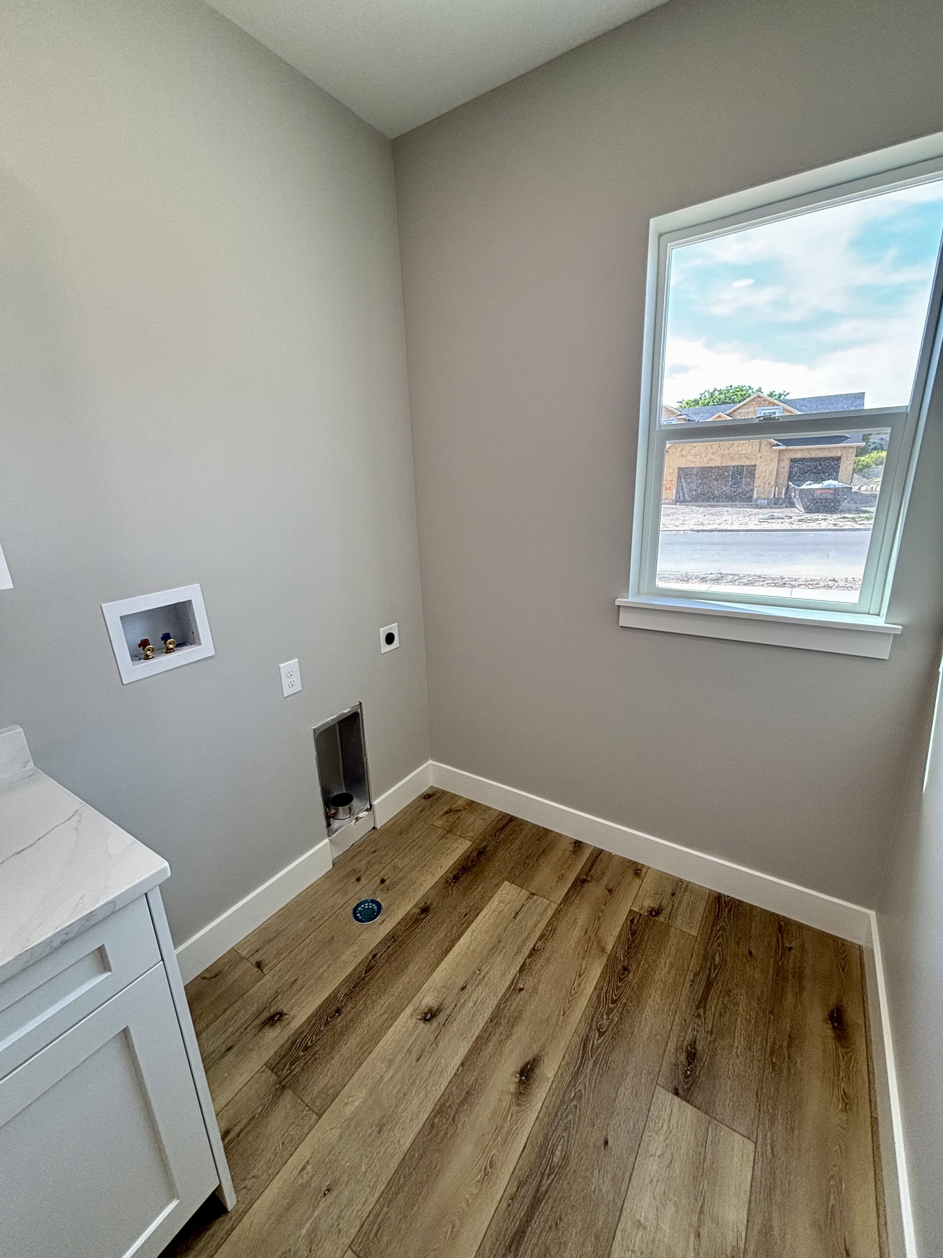 Laundry area featuring lvp wood style flooring, light gray walls, a window with white trim, and a built-in cabinet with a light quartz countertop